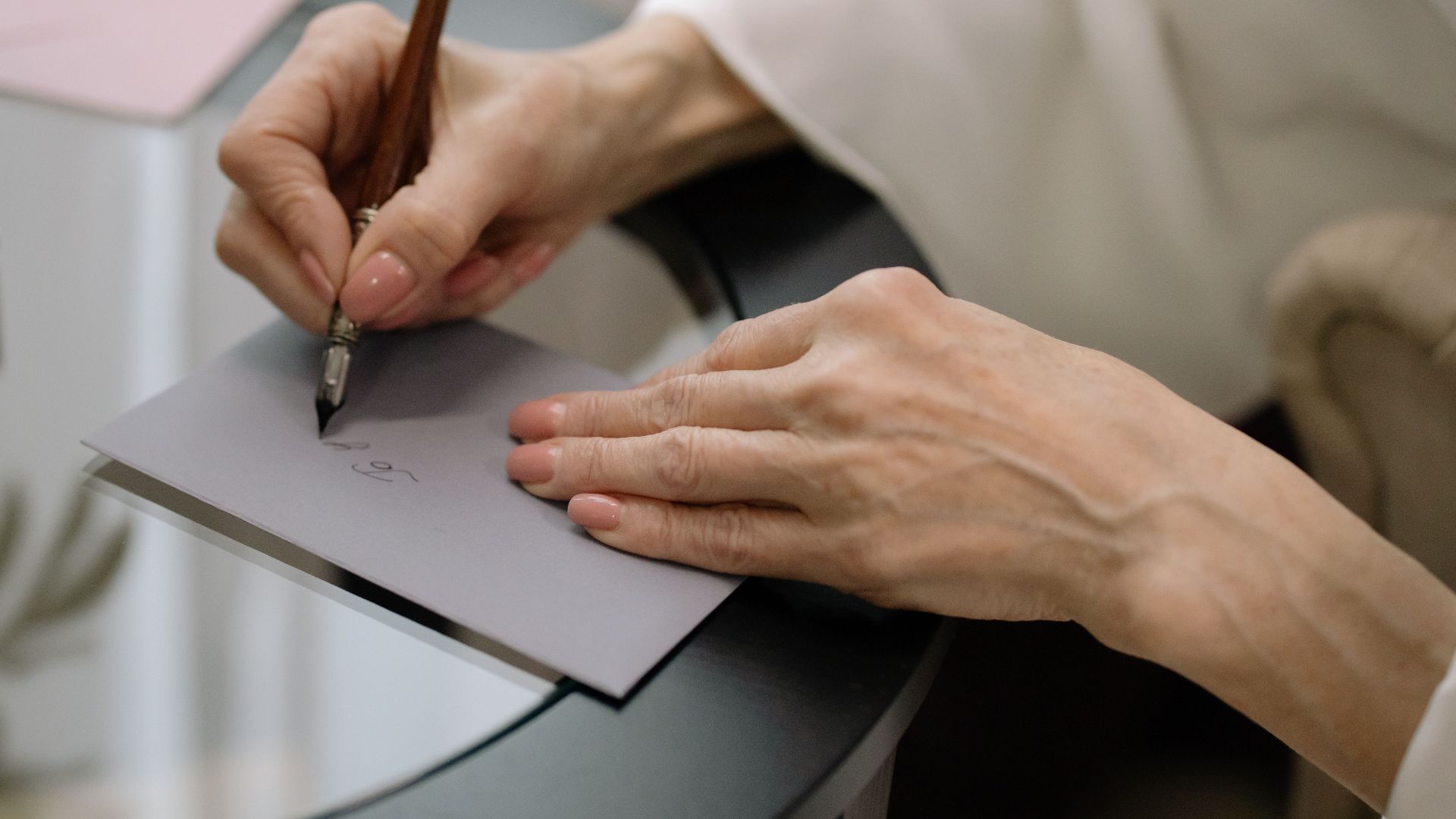 Close-up of hands elegantly writing on a gray envelope using a fountain pen.
