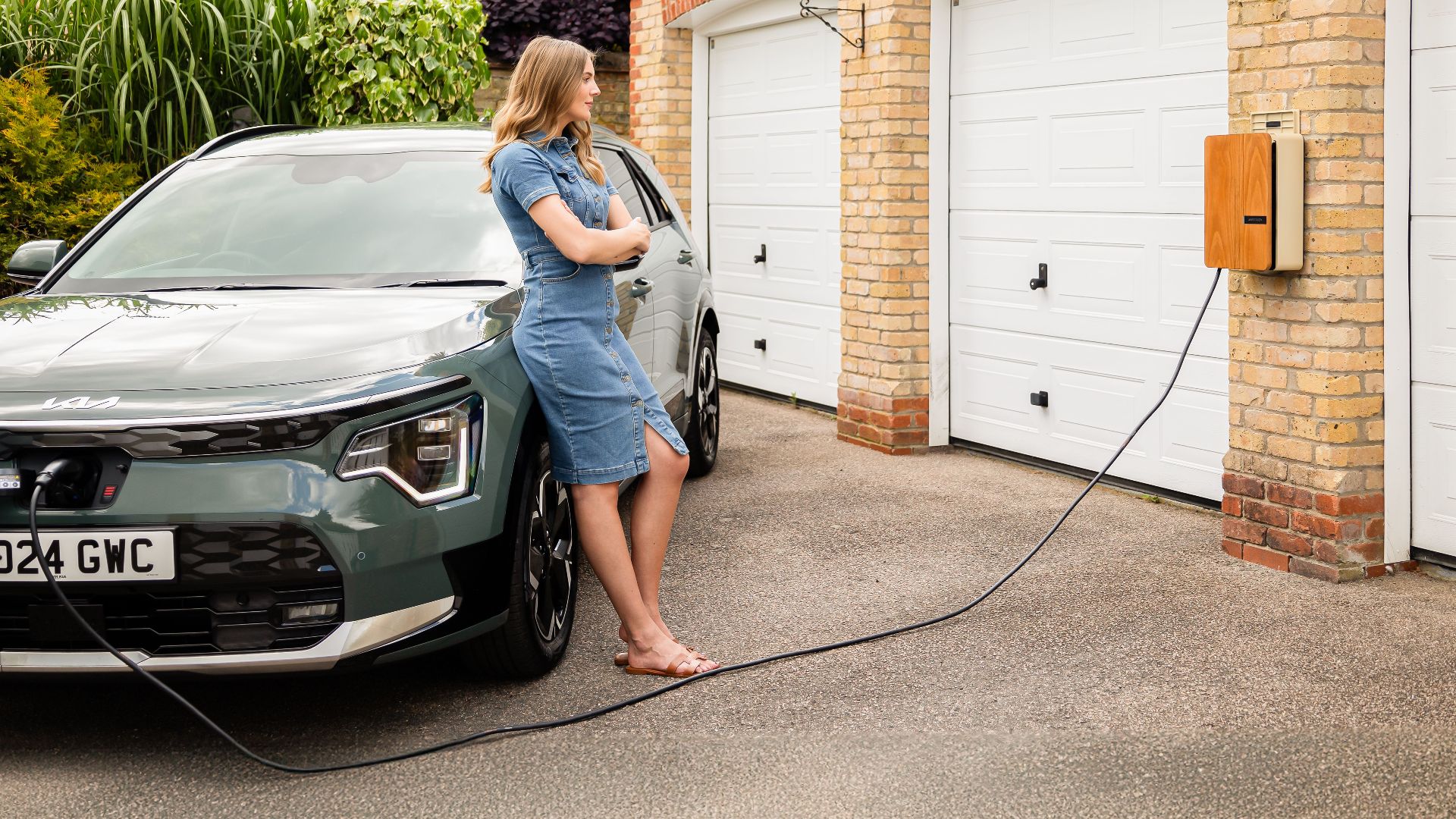 Woman charging electric vehicle at home with a modern wall-mounted charging station.