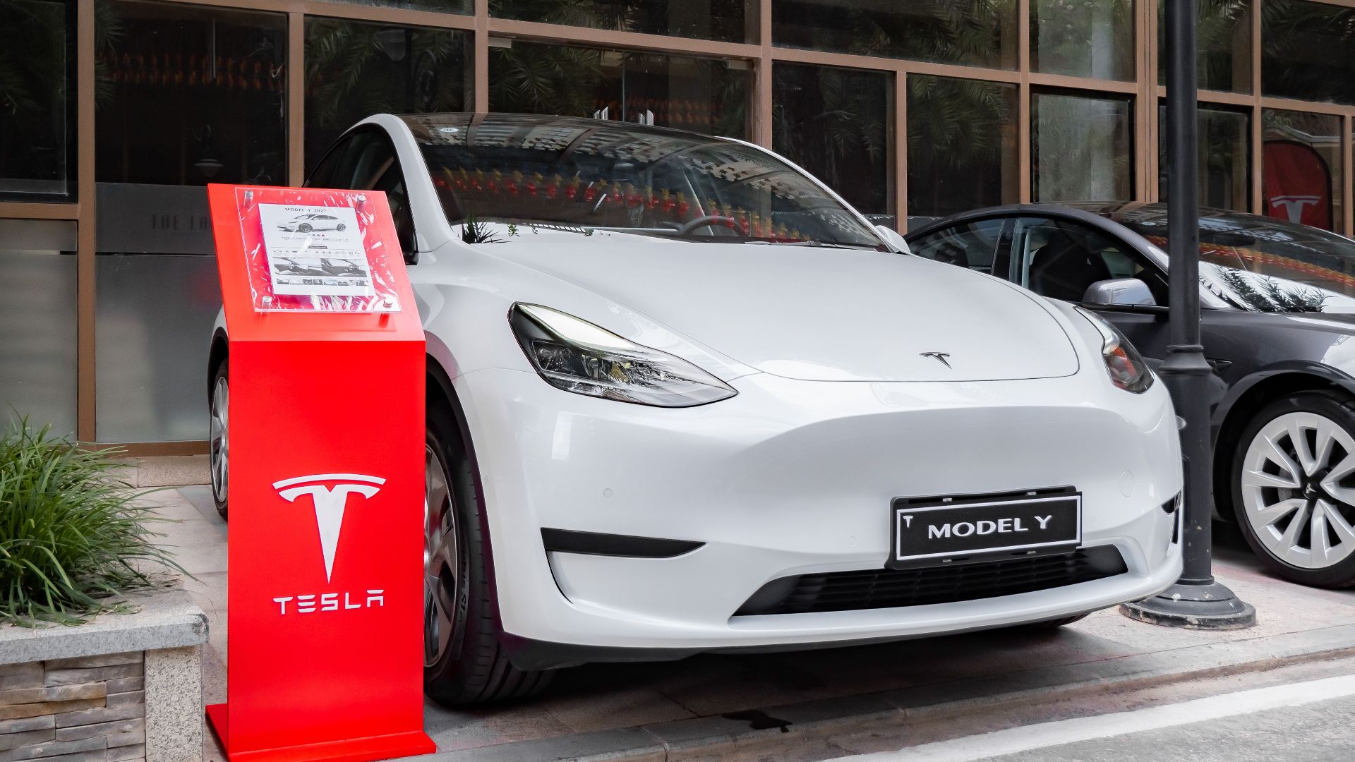 Tesla Model Y parked outdoors with a red display stand in front. Modern and sleek automotive design.