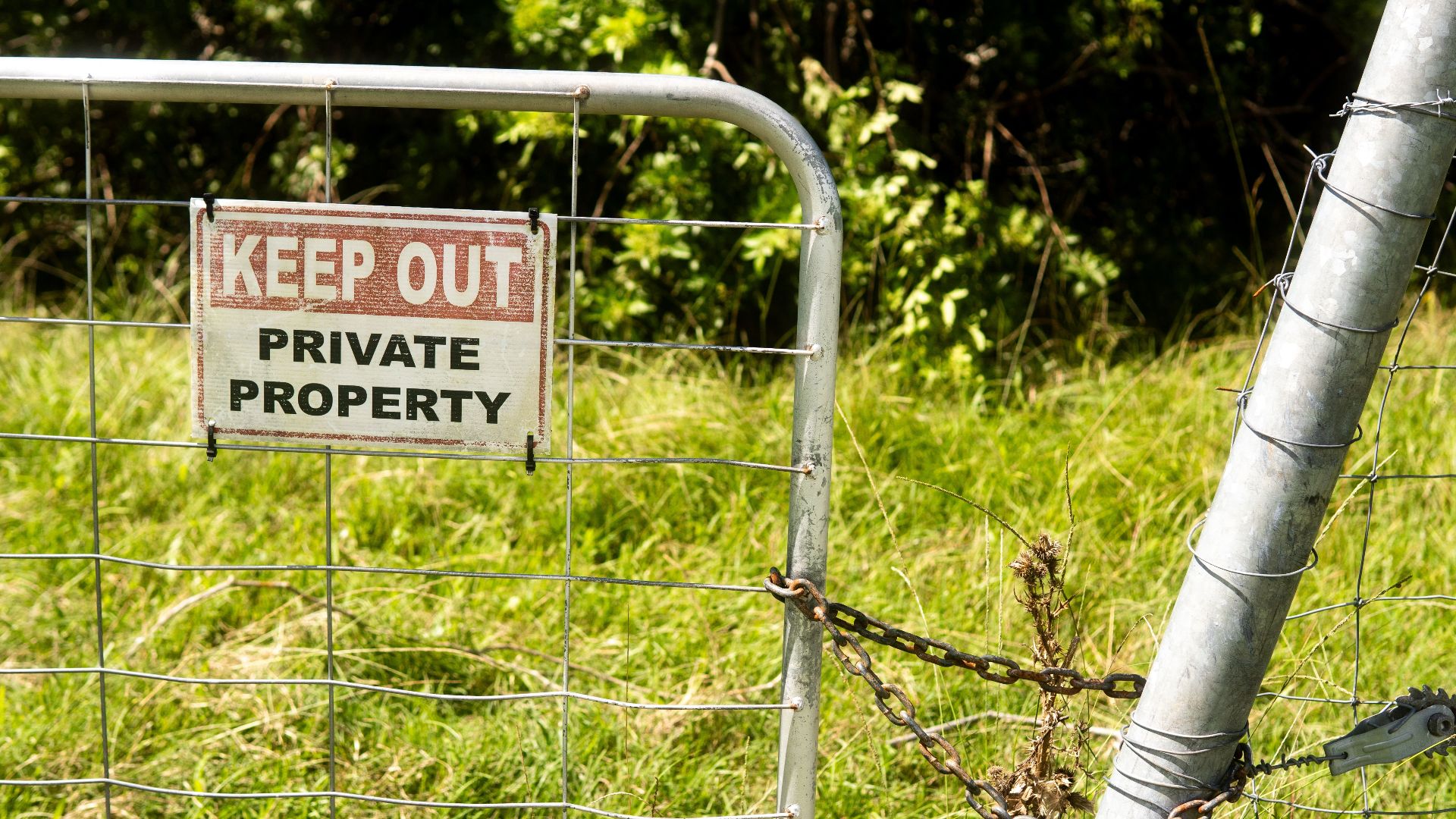 Metal fence with 'Keep Out Private Property' sign in a grassy outdoor setting.