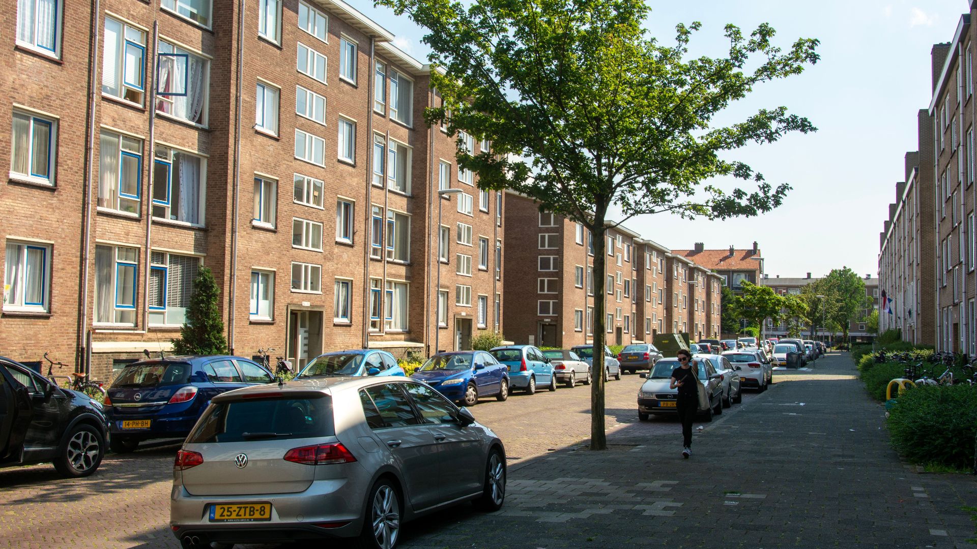 Urban street with parked cars and residential buildings on a sunny day.
