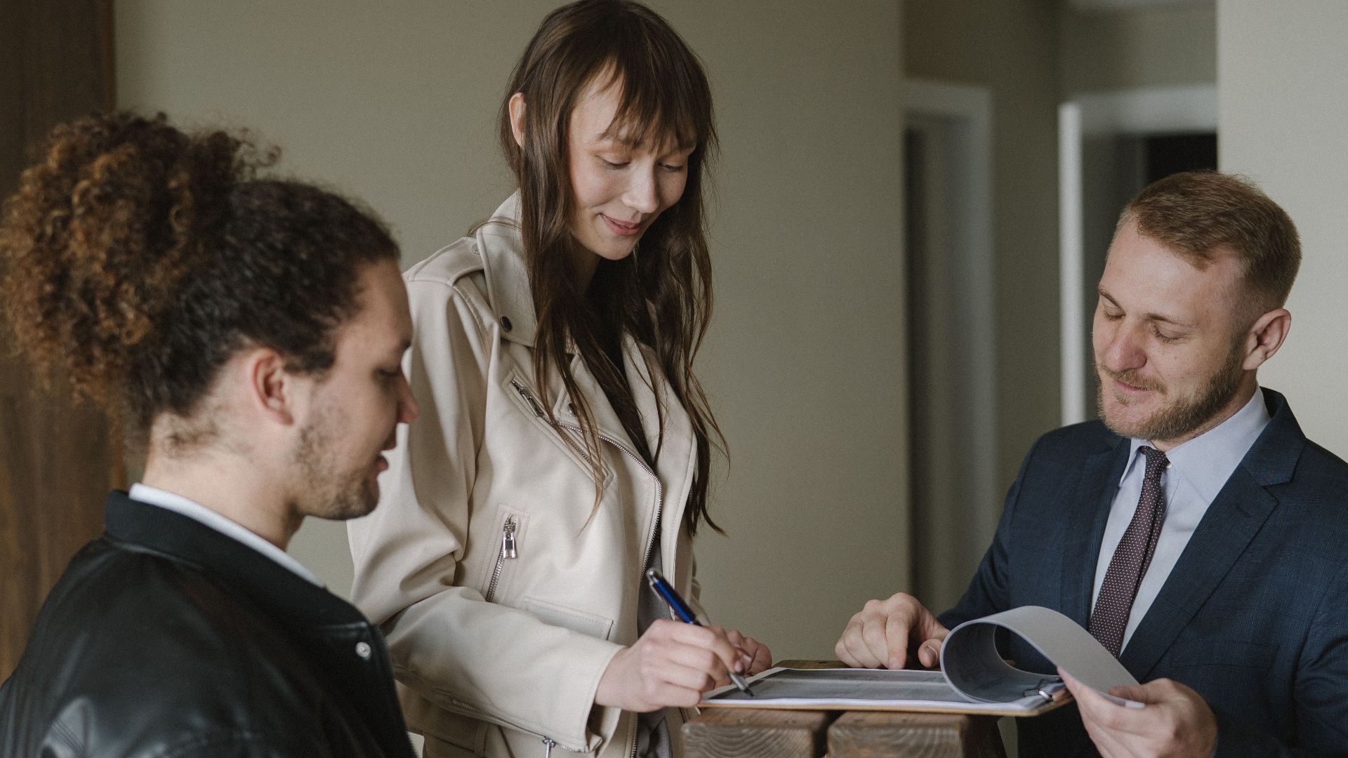 A couple signing real estate documents with a realtor inside a new apartment.