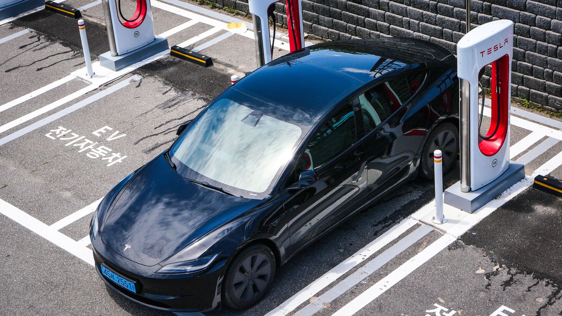 A black Tesla parked at a charging station in an urban setting.