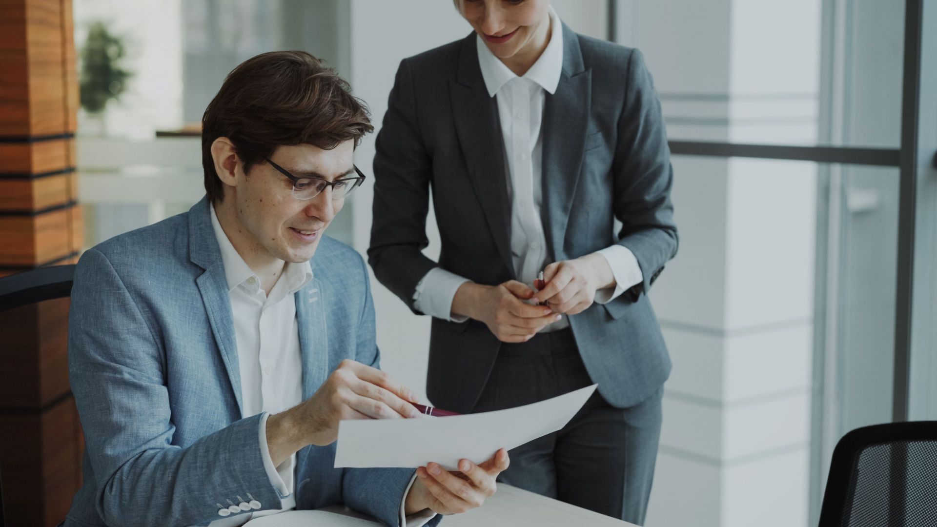 Two business professionals discussing a document in a modern office setting.