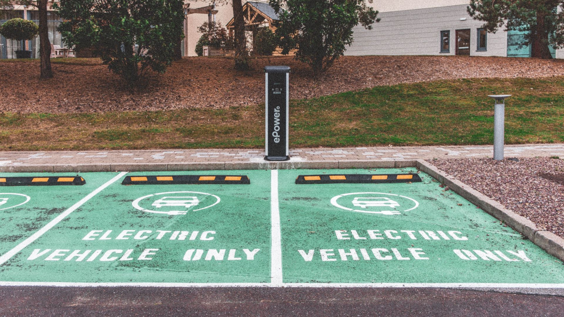 Green electric vehicle parking with charging station in urban environment.