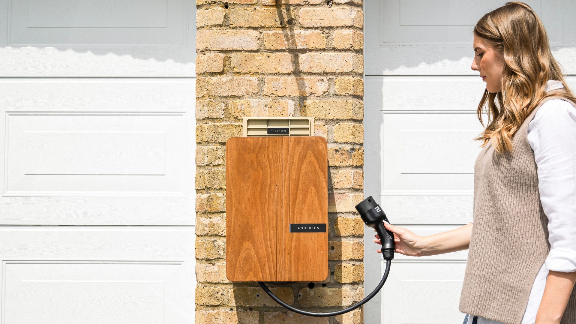 A woman uses a home electric vehicle charger mounted on a brick wall.