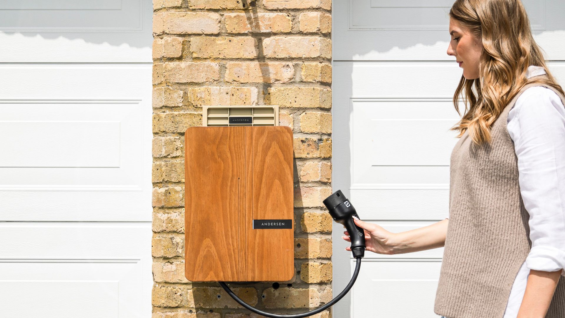 A woman uses a home electric vehicle charger mounted on a brick wall.