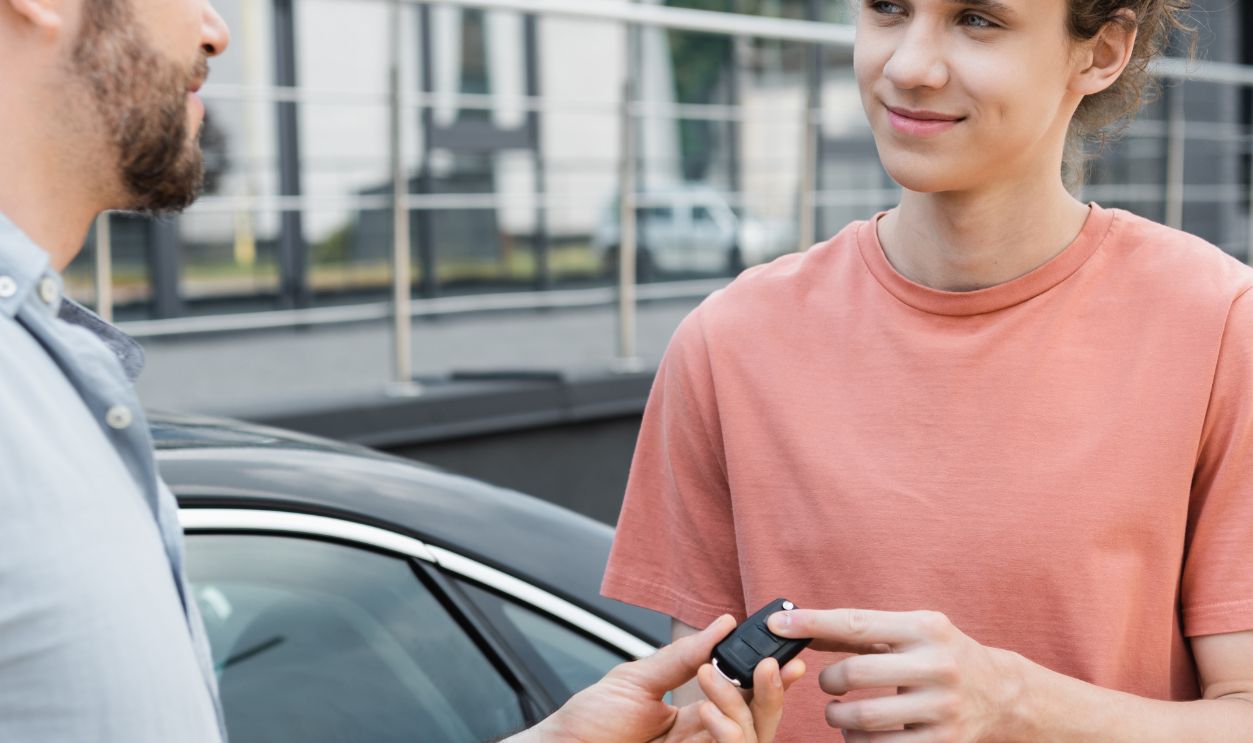 Shutterstock-2297935861, happy bearded man giving car key to cheerful teenage son near automobile