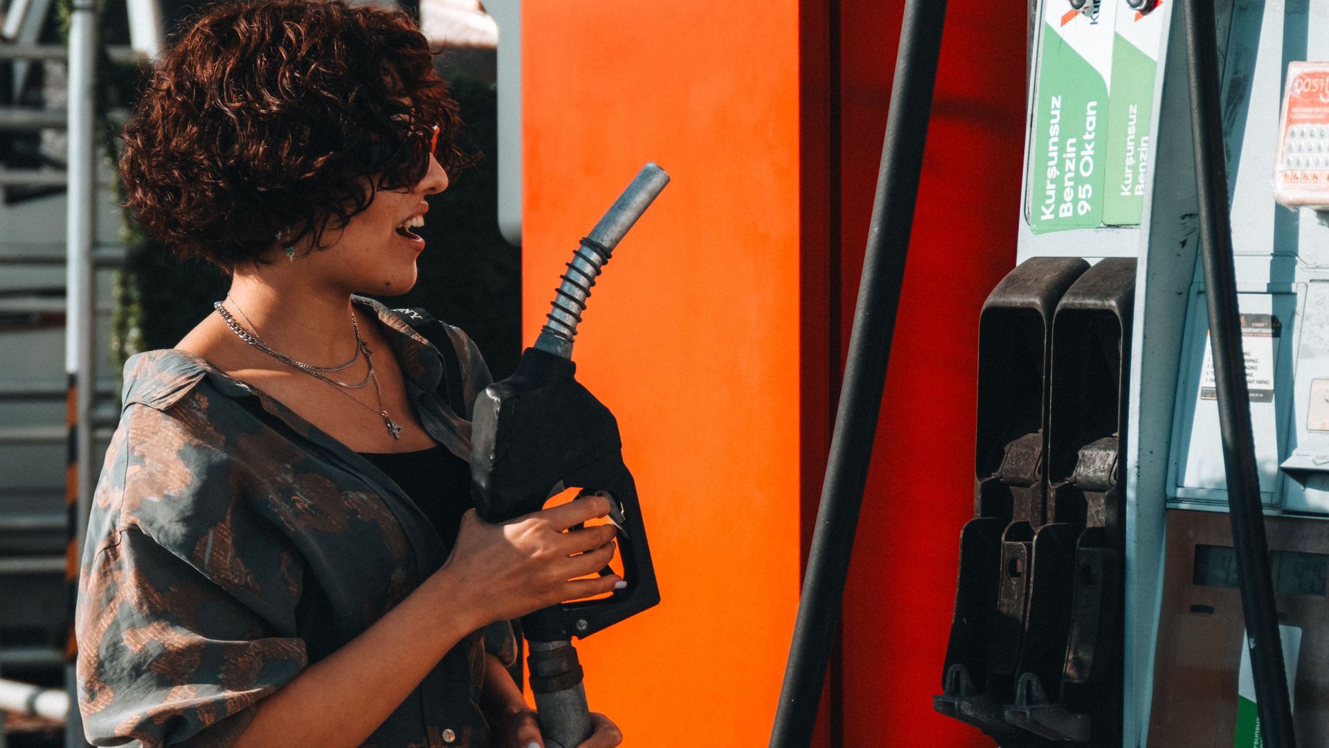 Woman refueling her car at a modern gas station during the day, under bright sunlight.