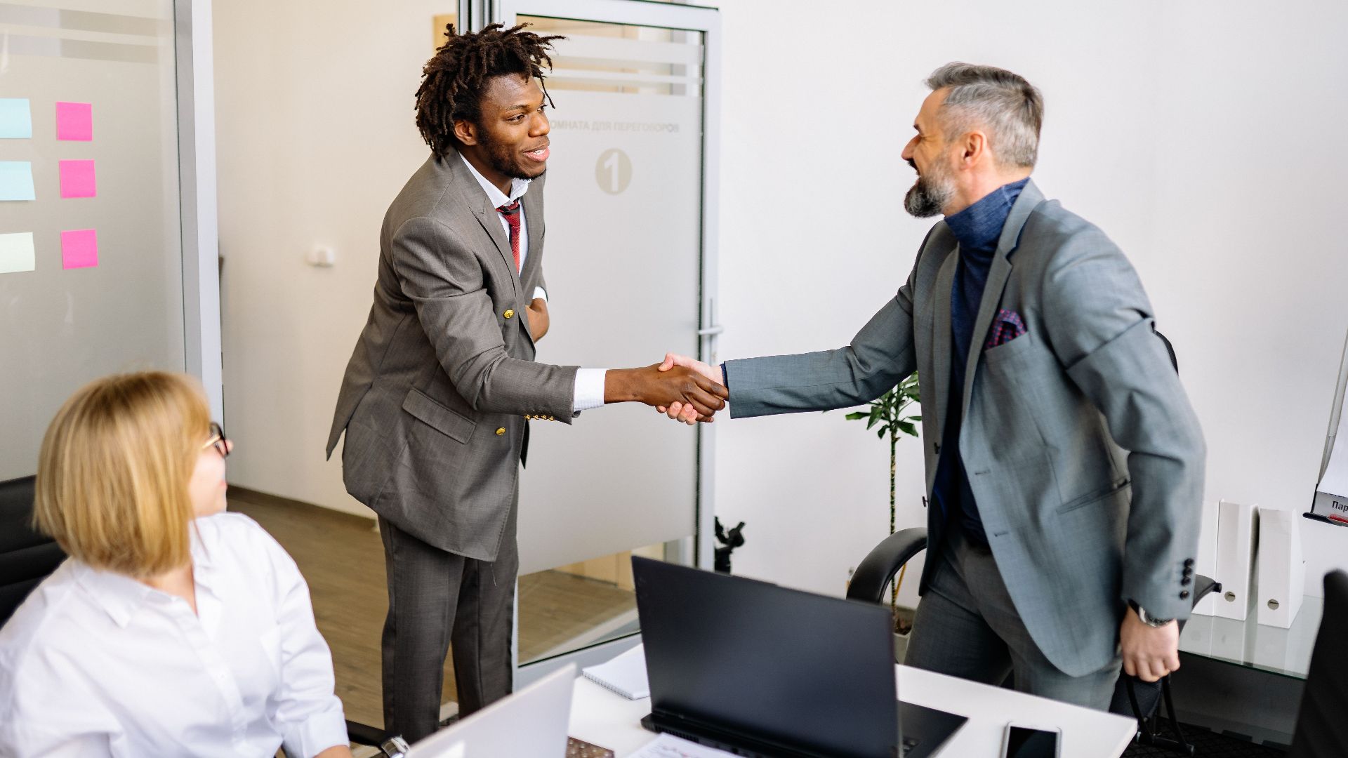 Two businessmen shaking hands in a modern office setting, symbolizing agreement.