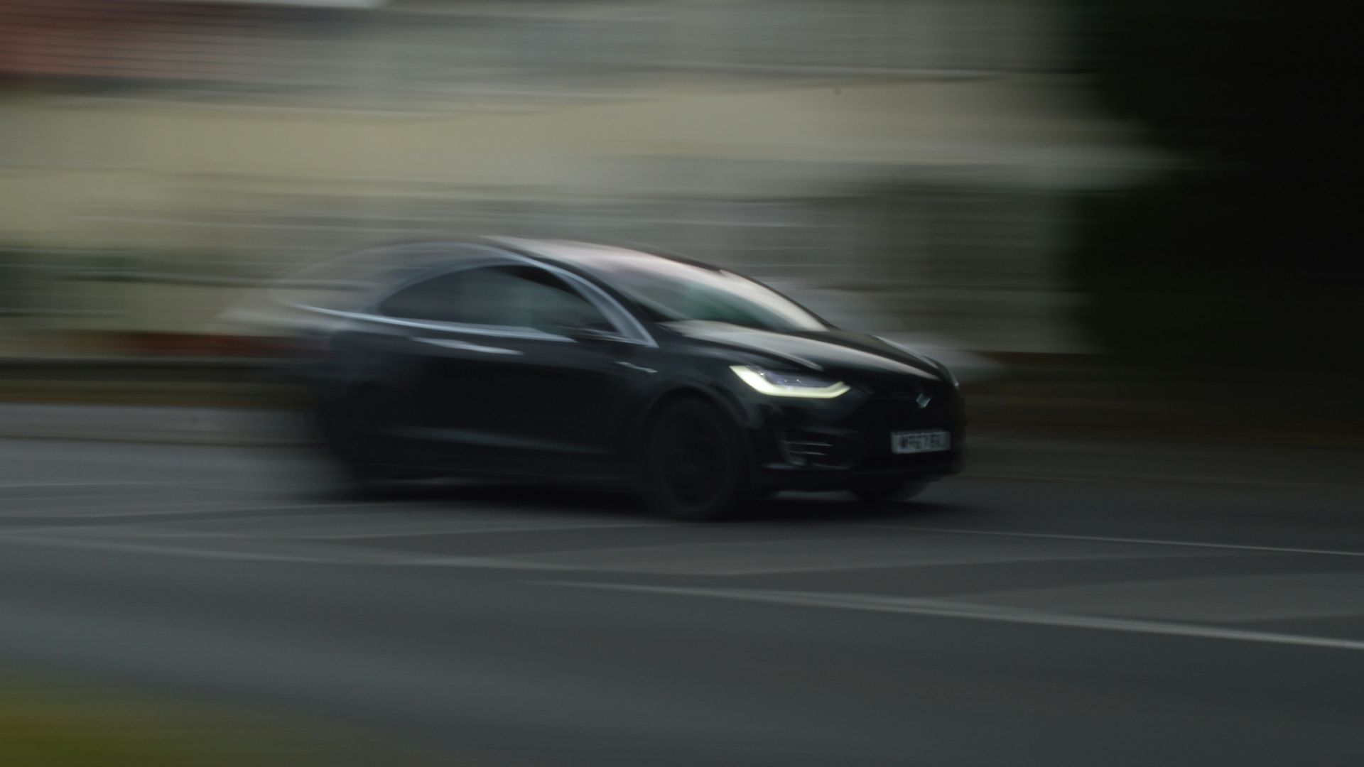 A black car speeds down a road with motion blur