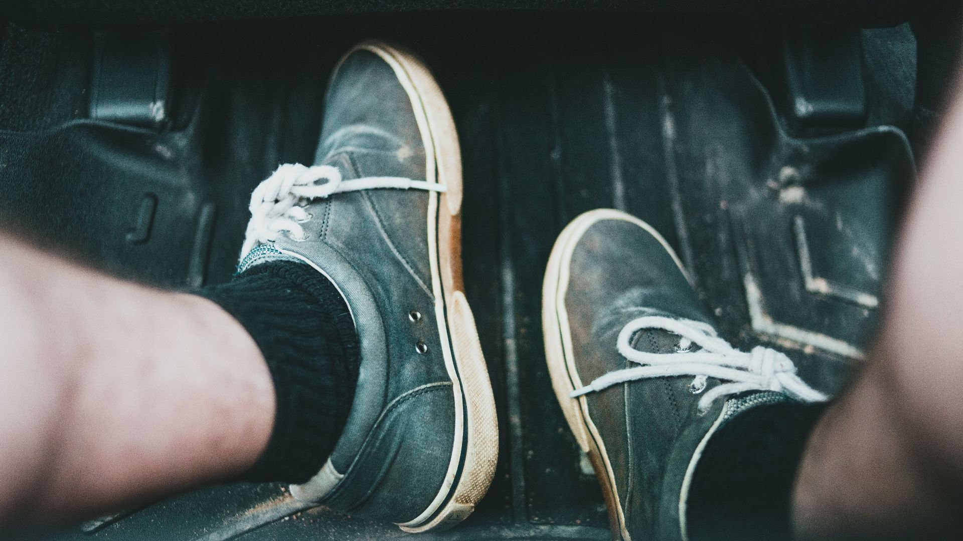 Close-up view of casual sneakers on a car's floor mat, highlighting footwear style and interior setting.