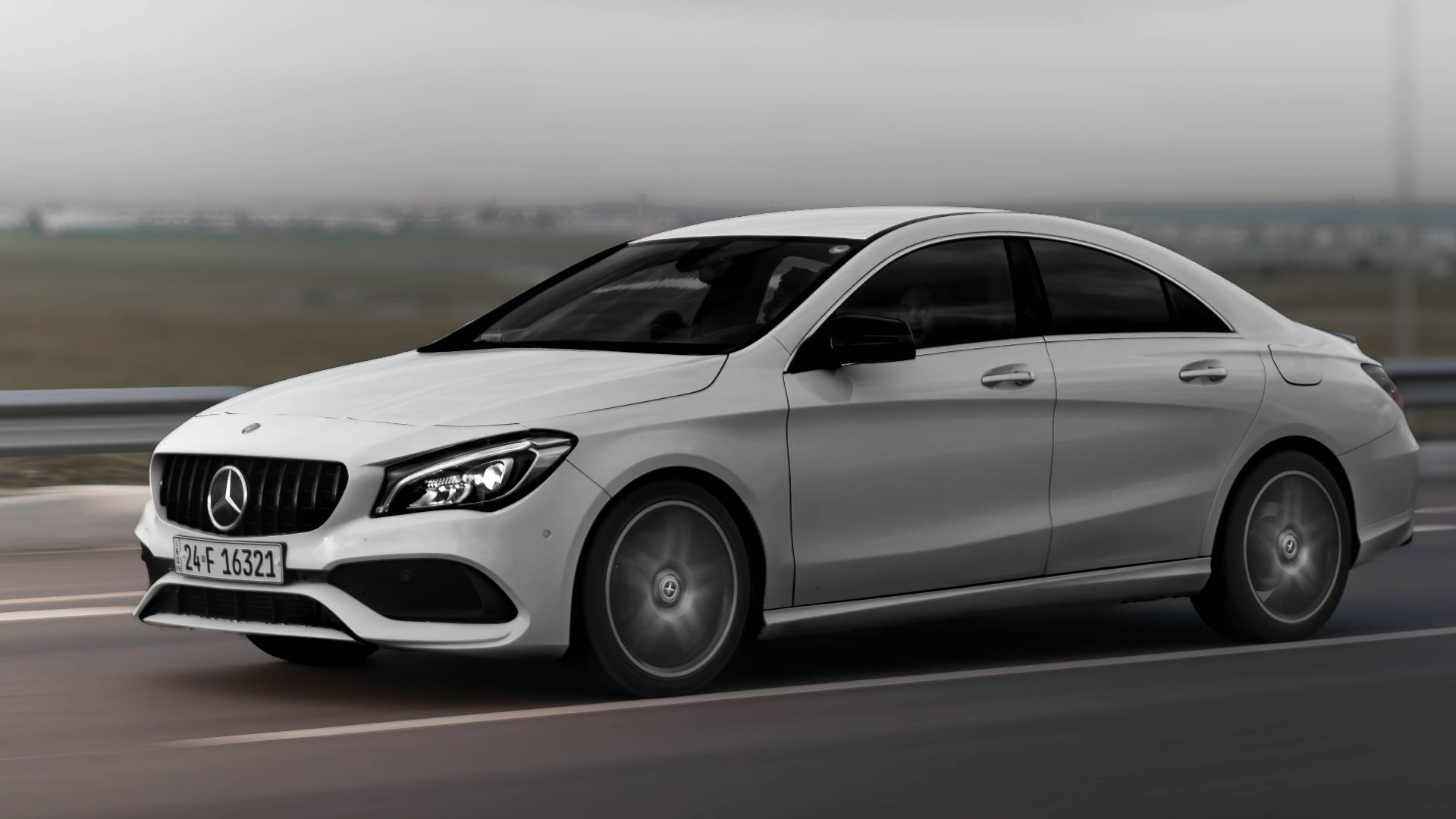 A sleek white sedan drives at speed on a highway under an overcast sky, captured in motion.