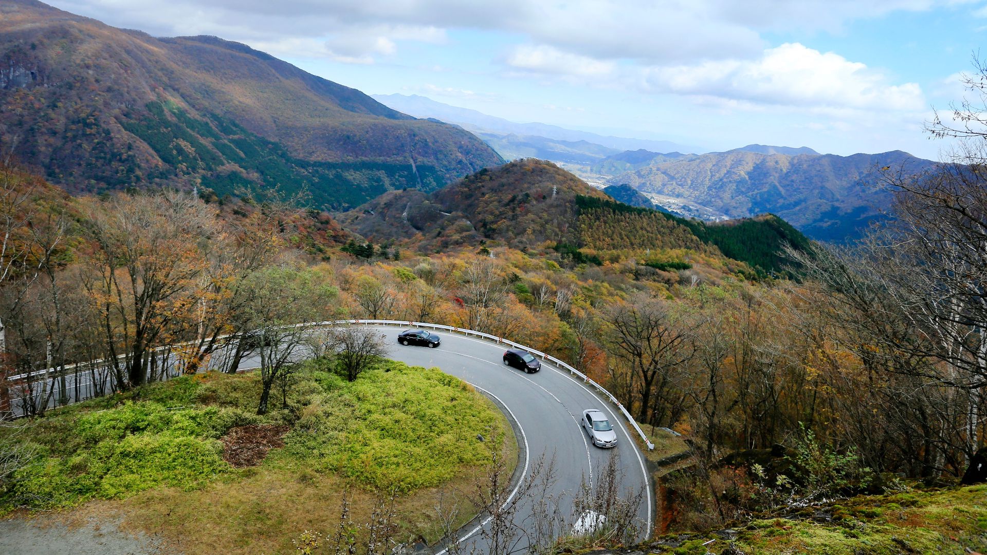 Curved mountain road with cars and stunning fall colors under a cloudy sky.