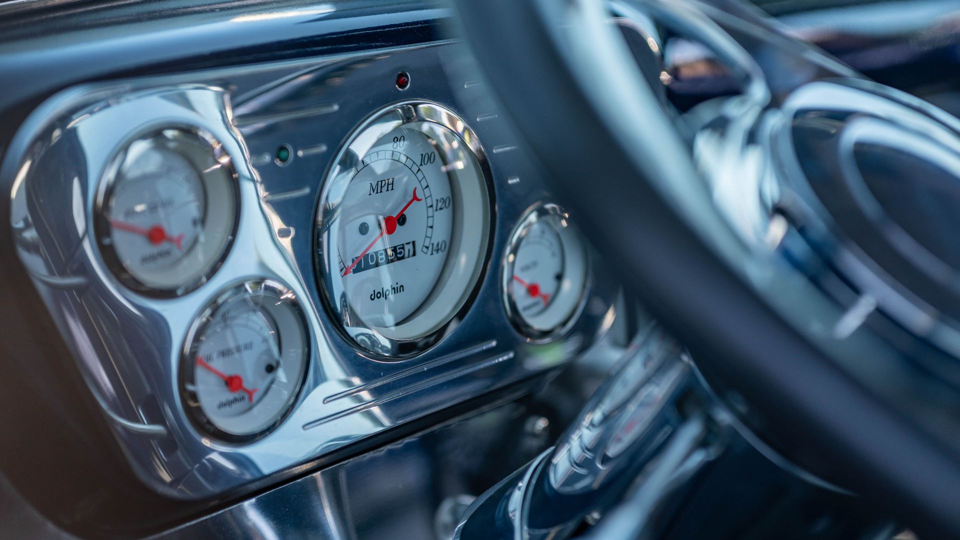 Detailed view of vintage car dashboard with chrome gauges and steering wheel, highlighting speedometer and odometer.
