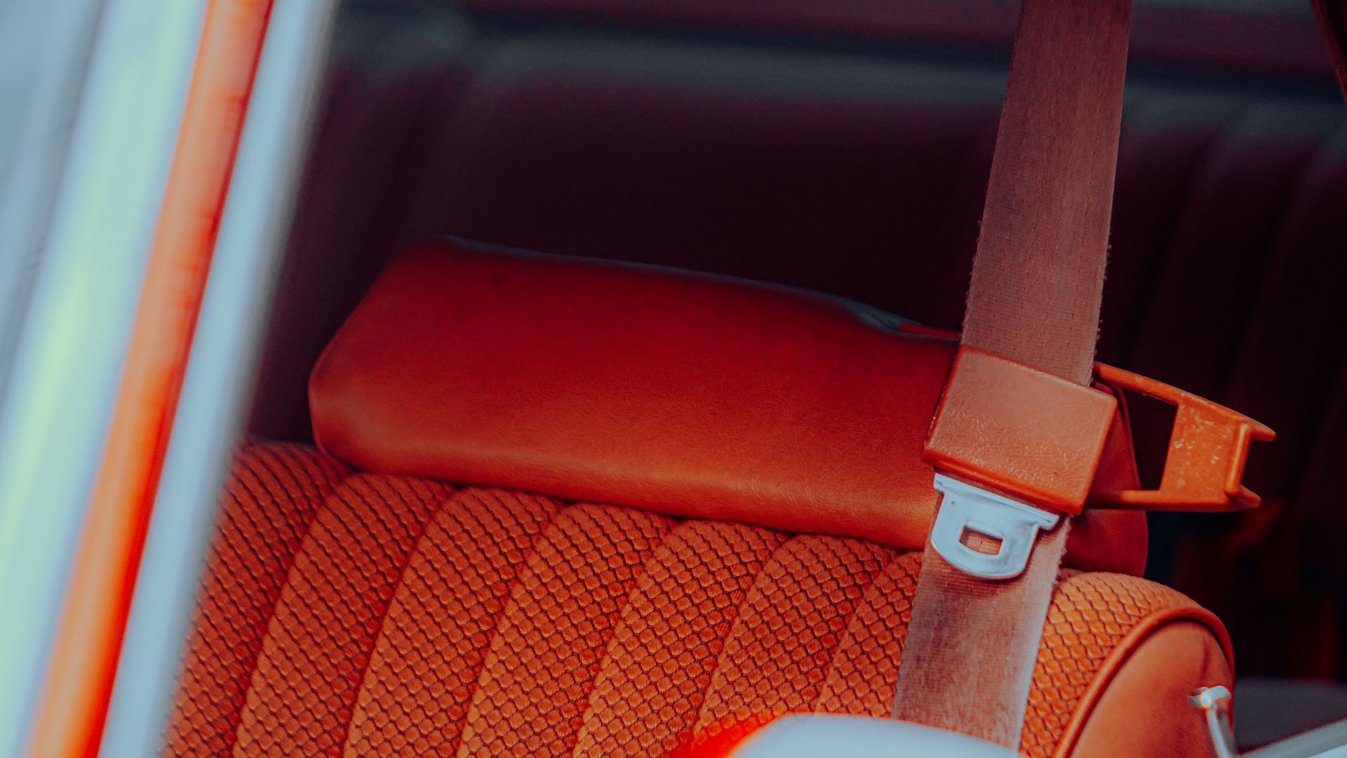 Close-up view of a vintage car interior showcasing a vibrant orange seat and seatbelt, exuding a retro vibe.