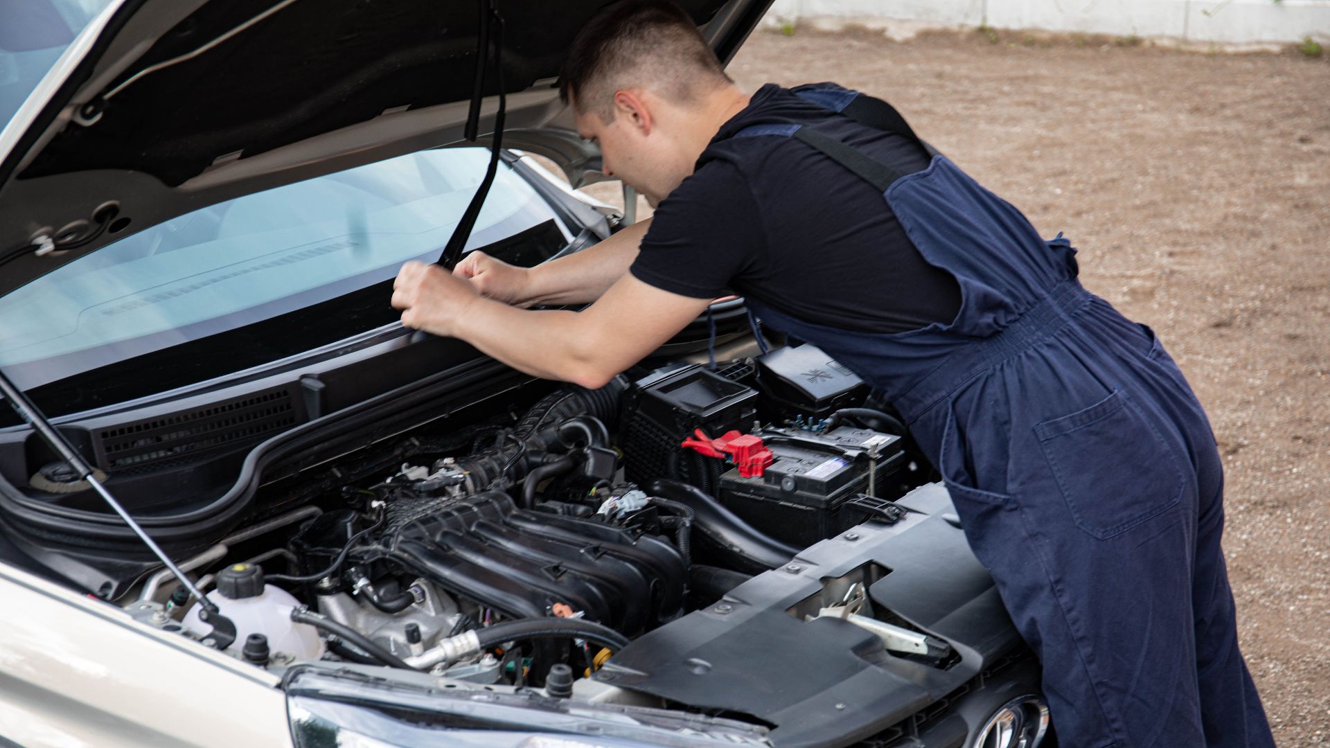 Mechanic working on a car engine with hood open, showcasing automotive repair skills.