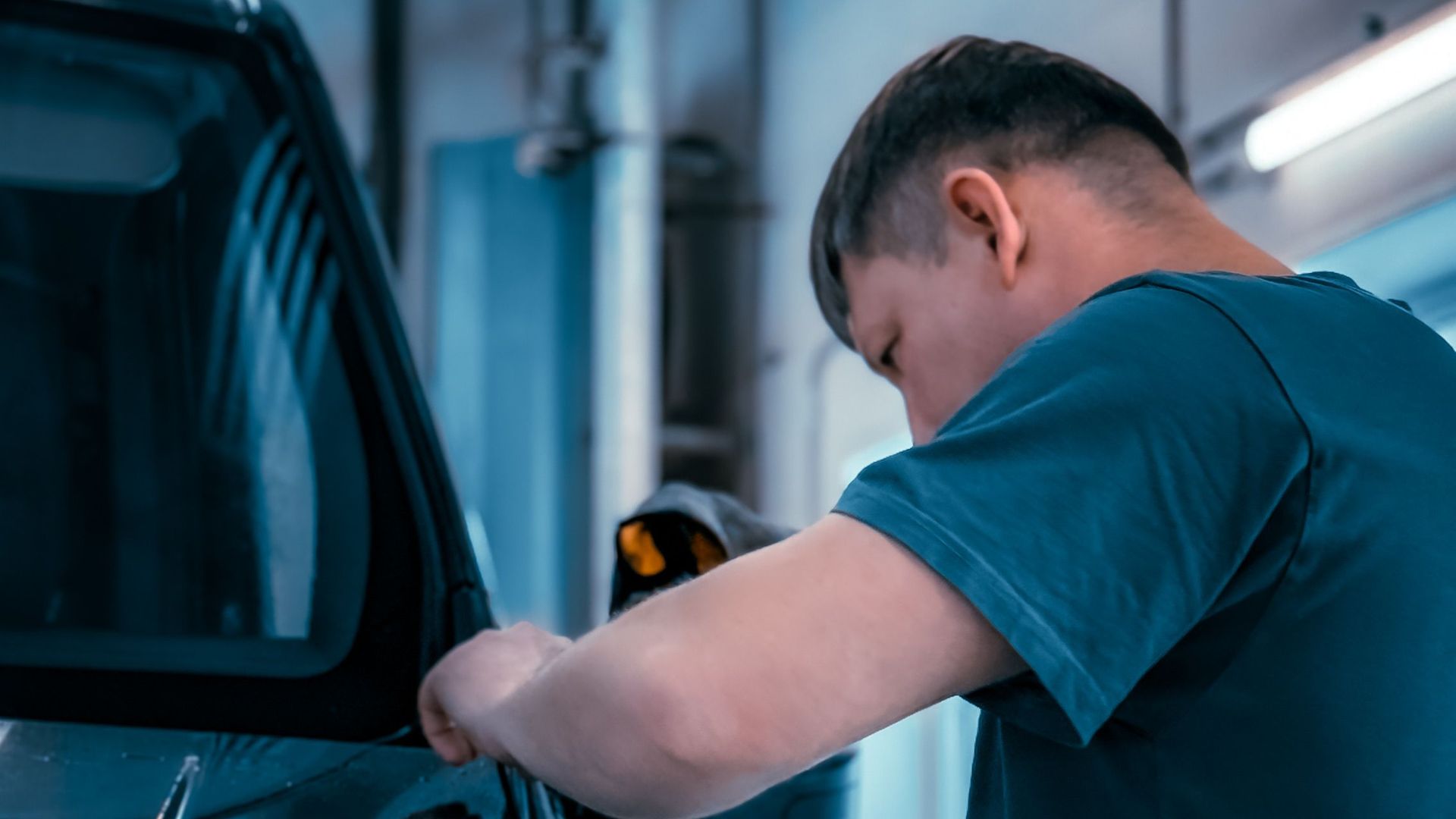 A mechanic focuses on fixing a car's side mirror in a well-lit garage.