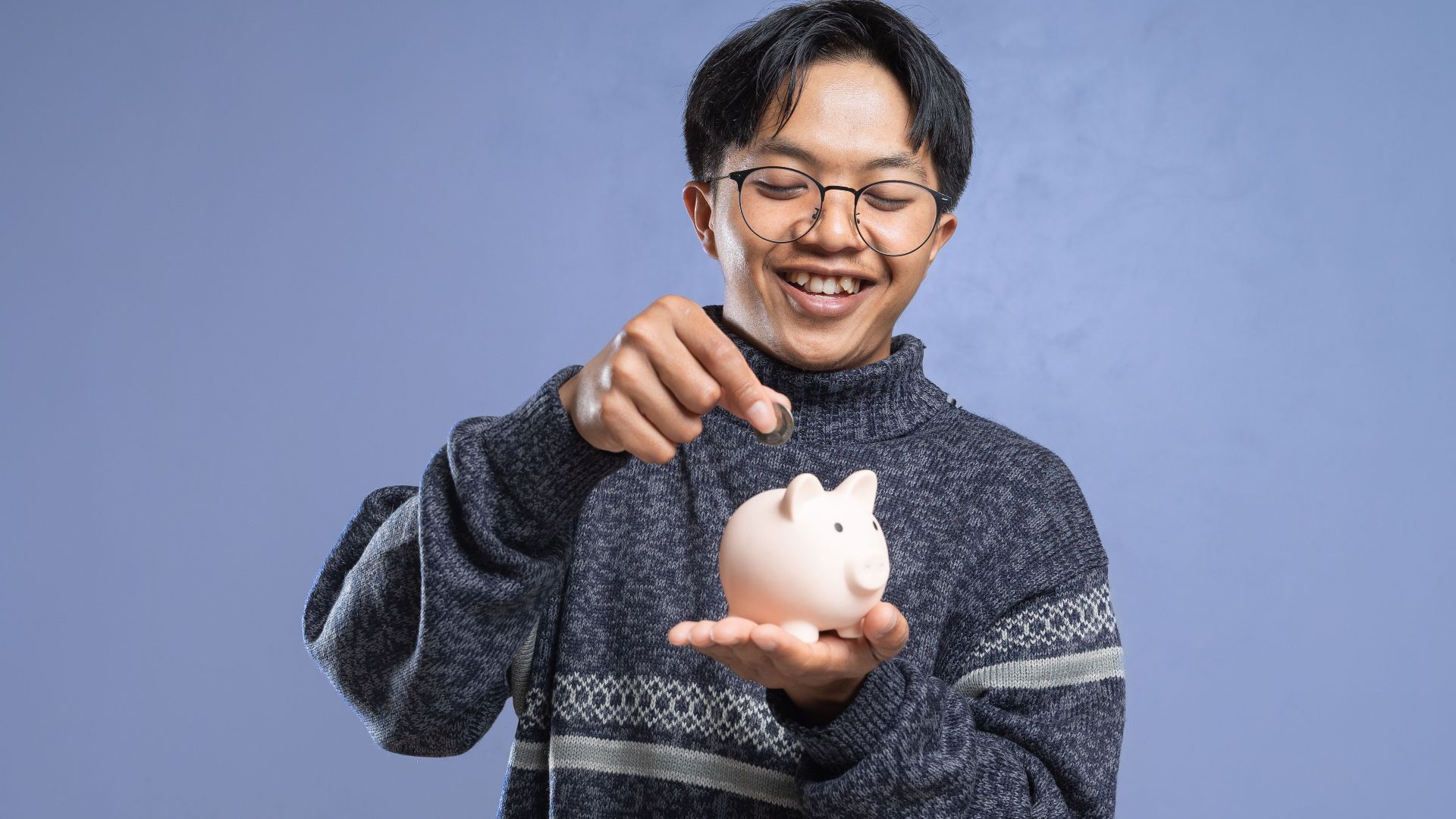 Smiling man holding a piggy bank and inserting a coin, representing savings and financial planning.