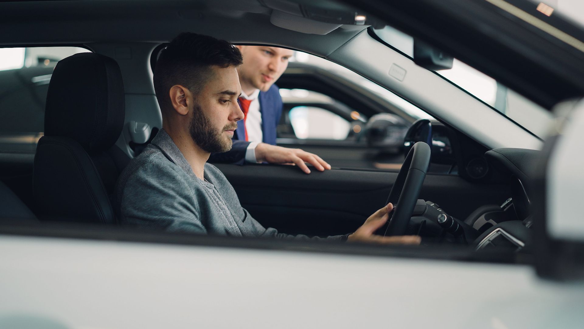 Man examining car interior with salesman at a dealership, highlighting car features.