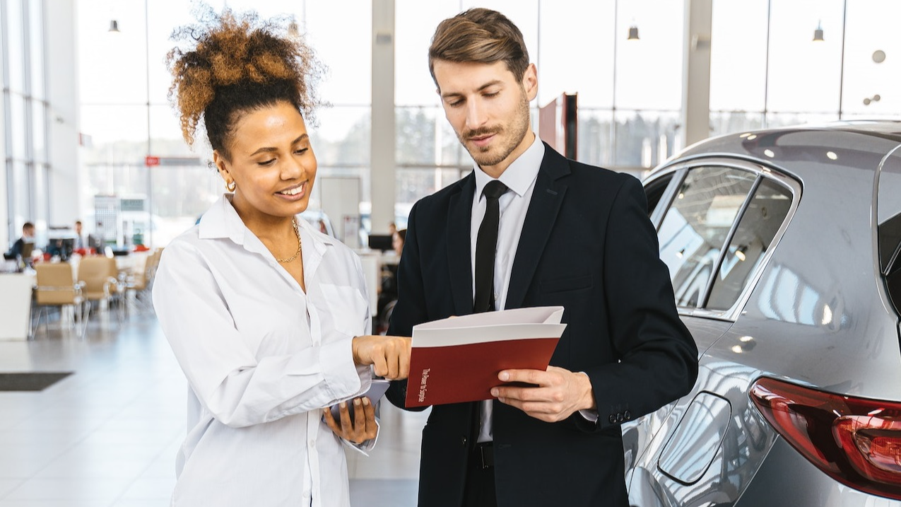 Man and woman are looking documents at car dealership.