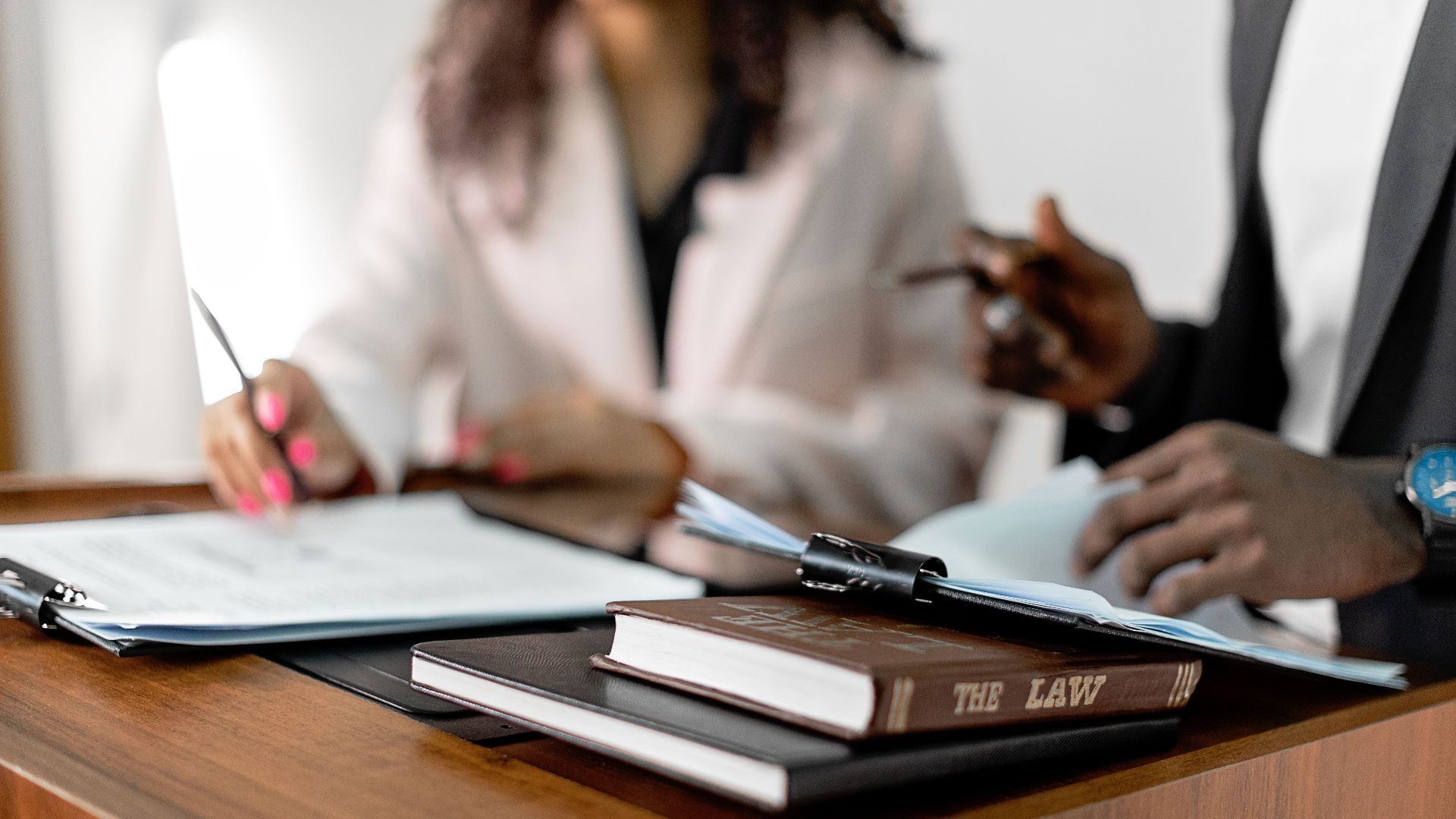 Two lawyers reviewing documents with law books on a desk. Professional legal environment.