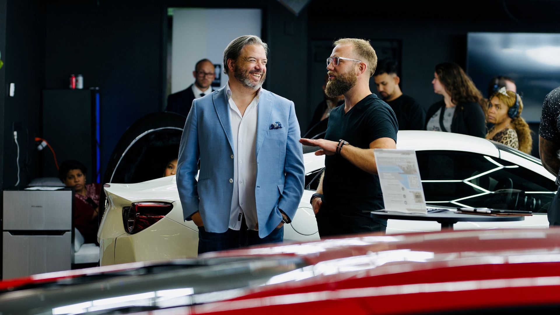 A luxury car event with attendees and videographers in a stylish Los Angeles showroom.