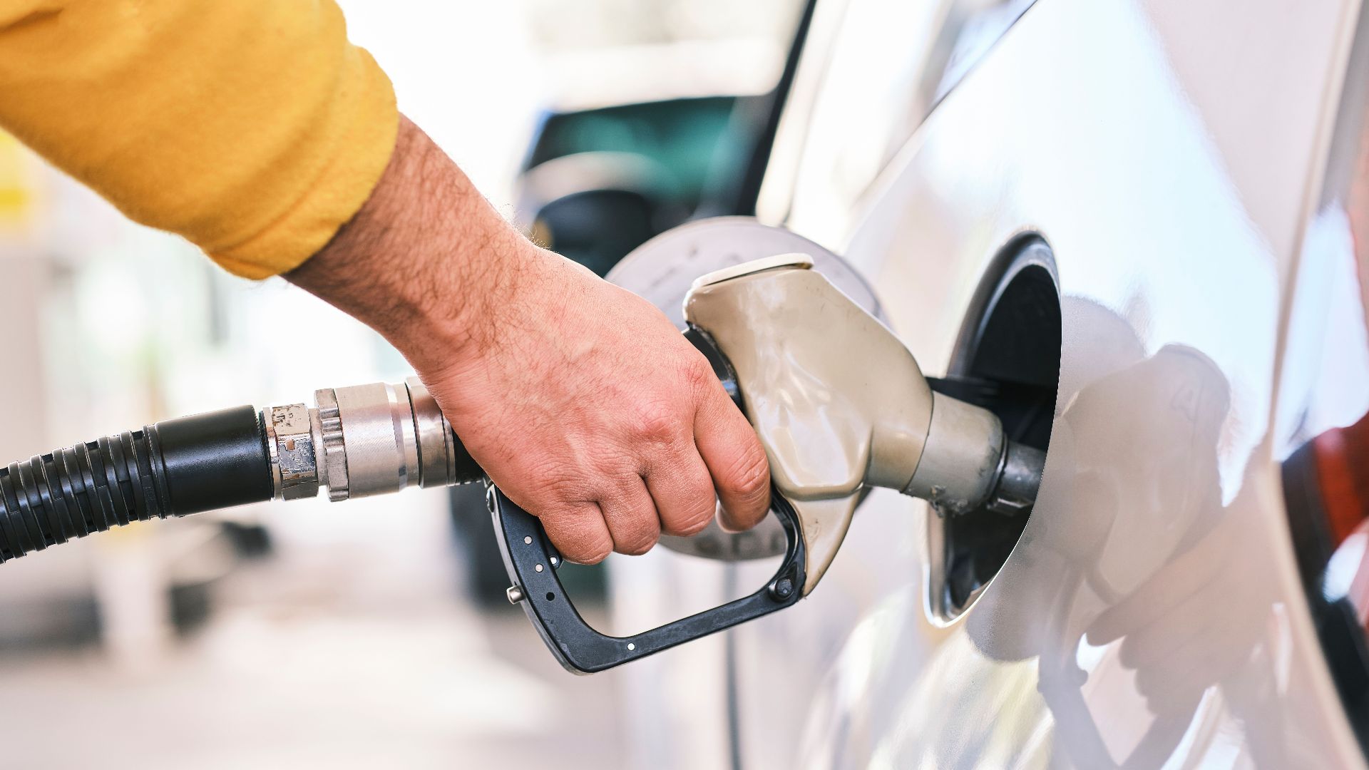 Close-up of a person refueling a car with a gas nozzle at a station.