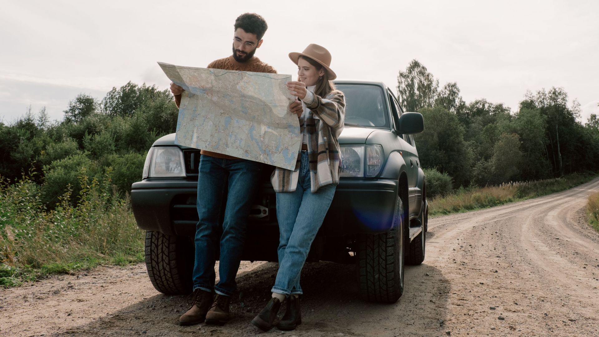 Couple reading a map beside their car on a rural road trip through lush greenery.