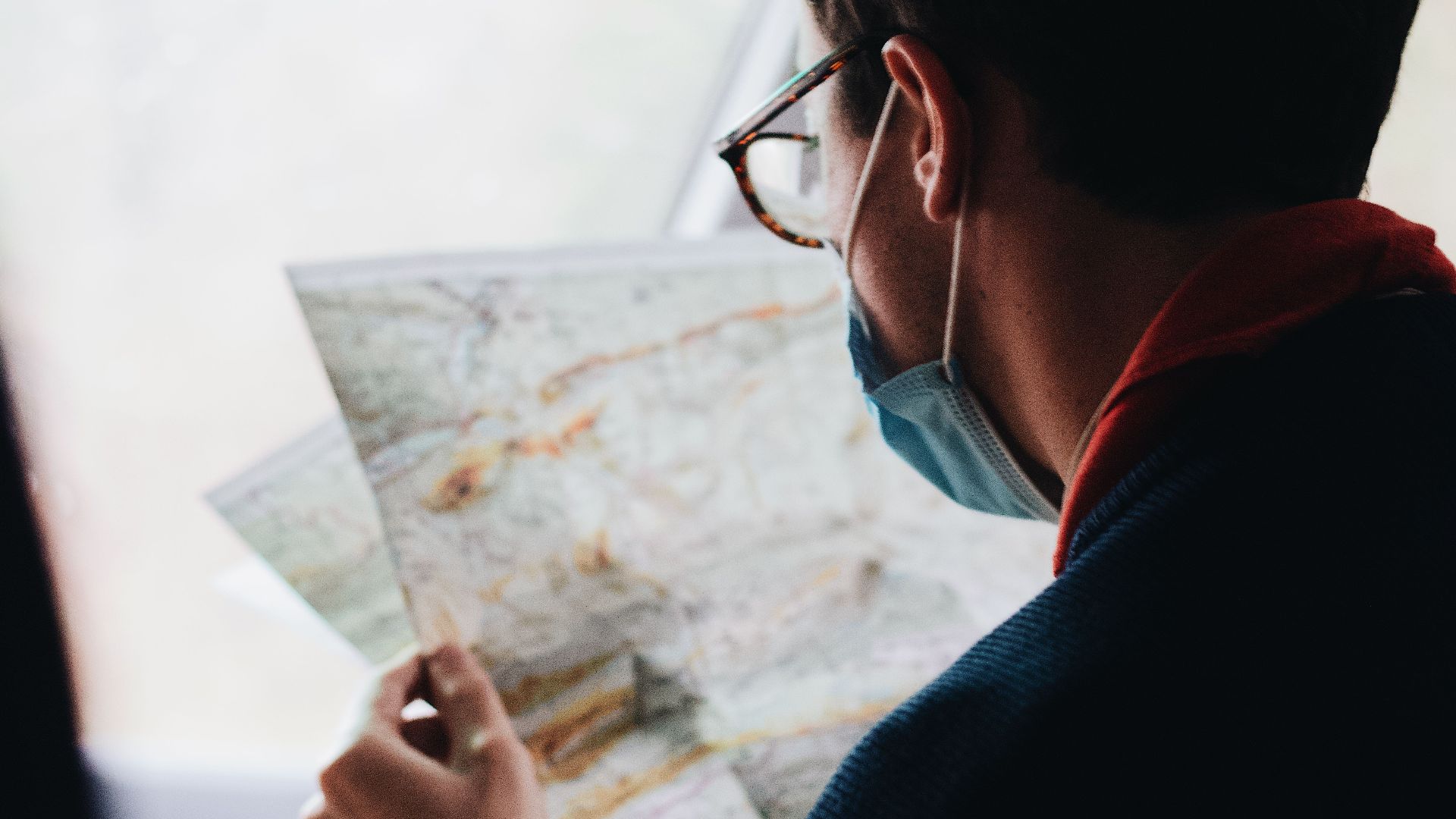 A man wearing a face mask examines a map while traveling in a vehicle during daytime.