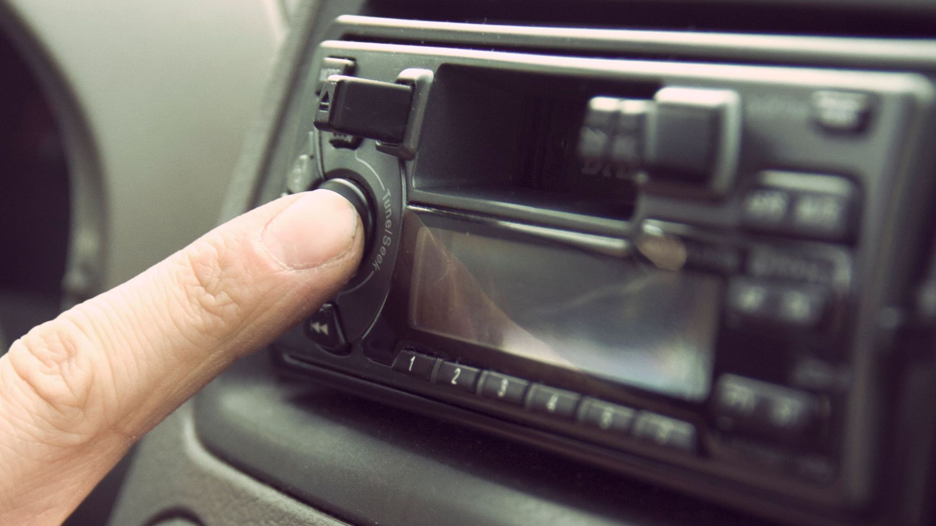 Finger adjusting car stereo in a vehicle's dashboard, depicting modern technology and music.