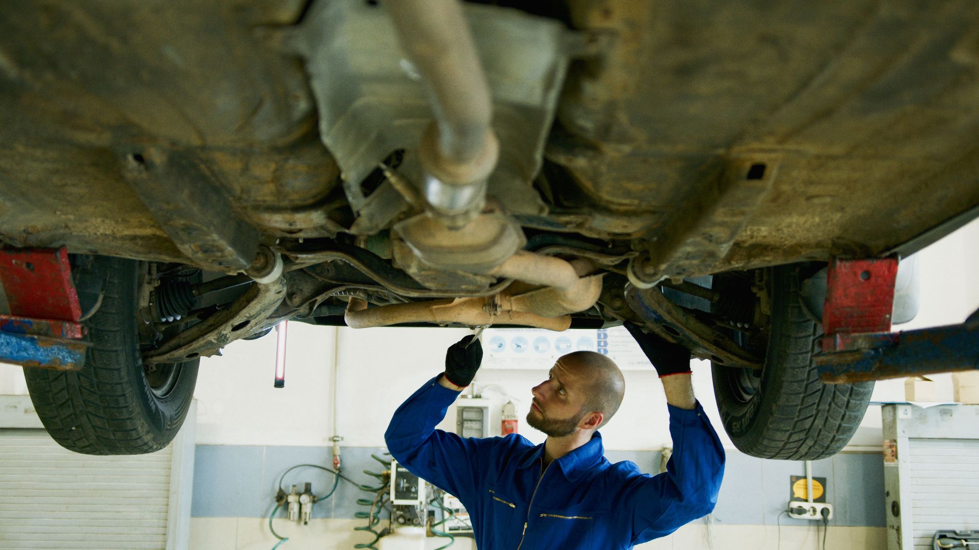 Mechanic examining the underside of a car in an auto repair shop for maintenance.