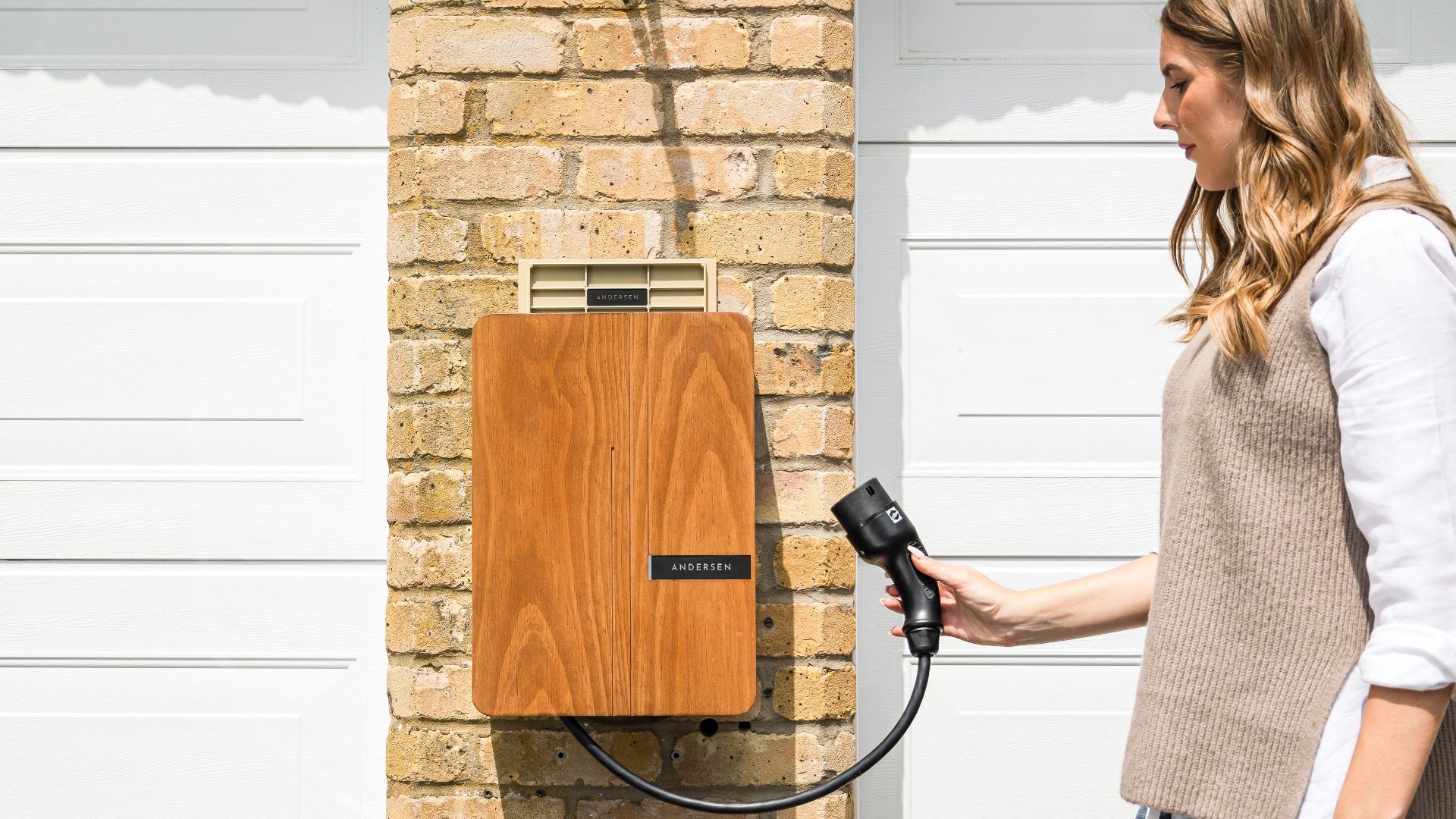 A woman uses a home electric vehicle charger mounted on a brick wall.