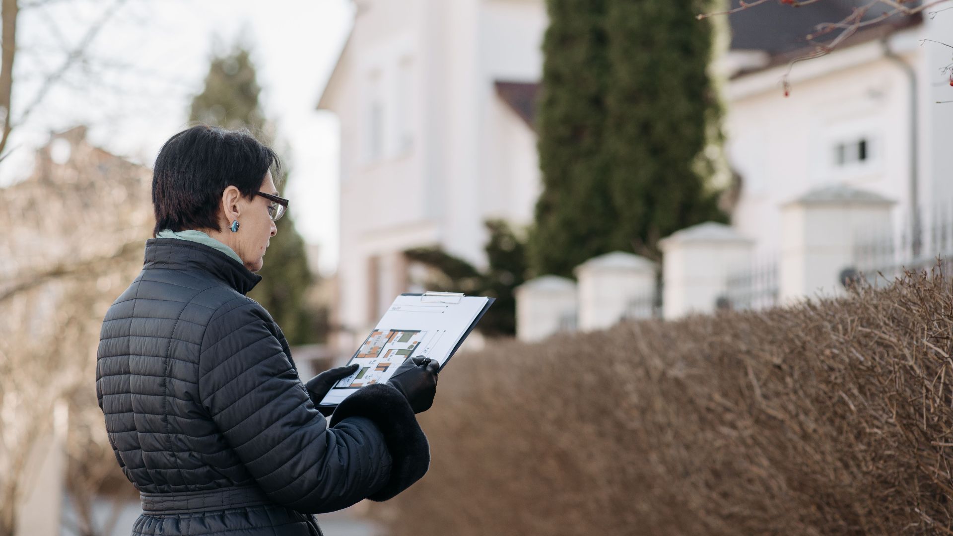 Realtor assessing house with clipboard during winter season outdoors. Ideal image for real estate content.