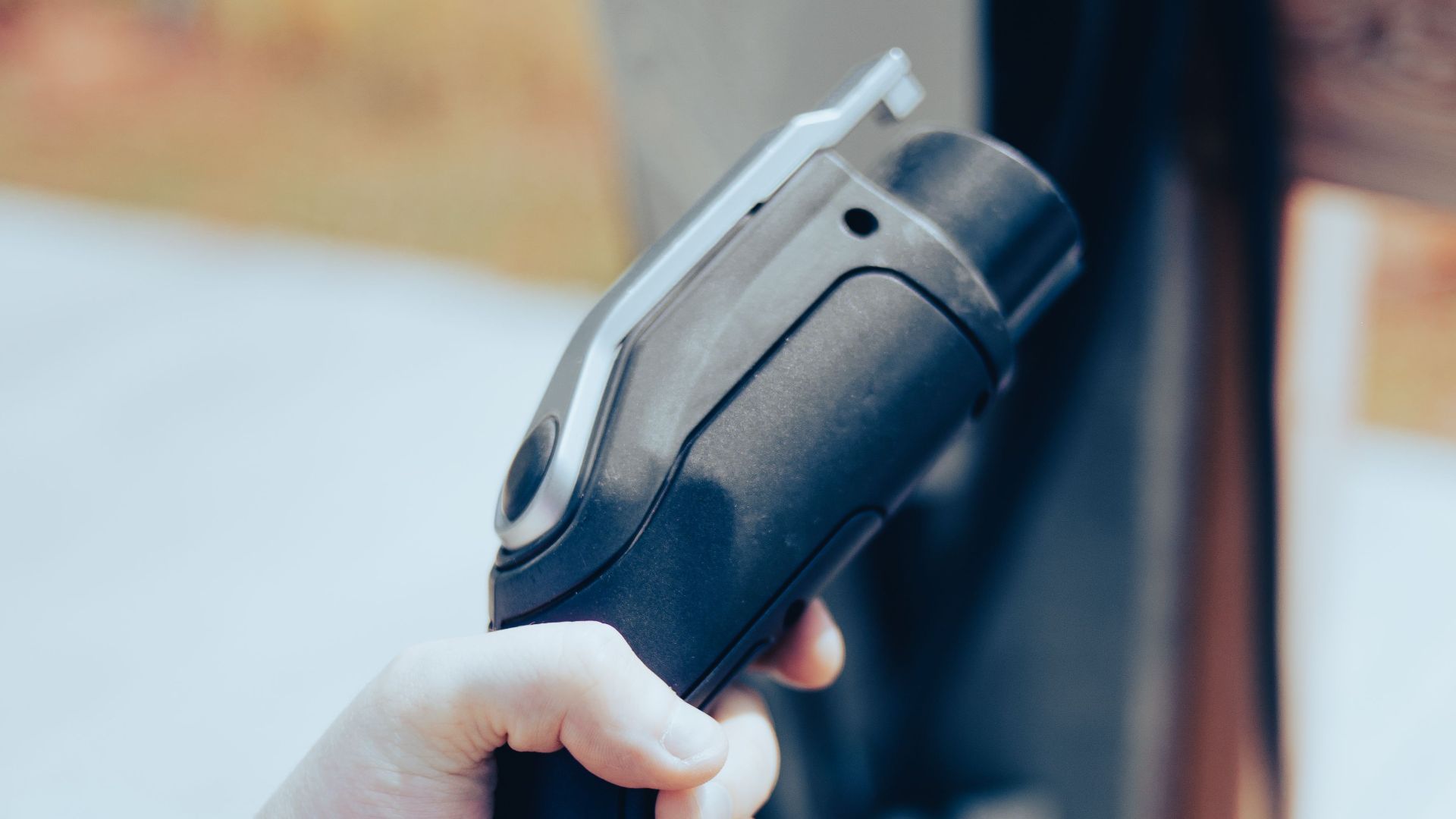 Close-up of a hand holding an EV charging cable outdoors, highlighting modern technology.