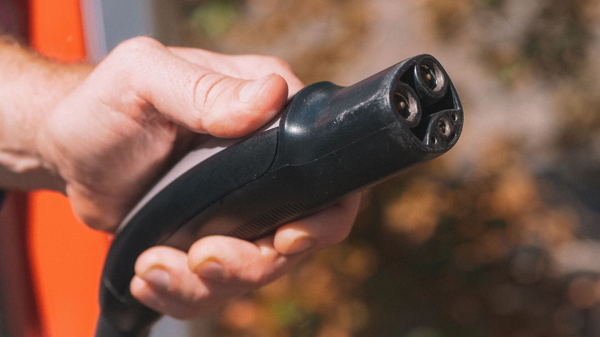 Hand holding an electric vehicle charging plug, symbolizing clean energy and innovation.
