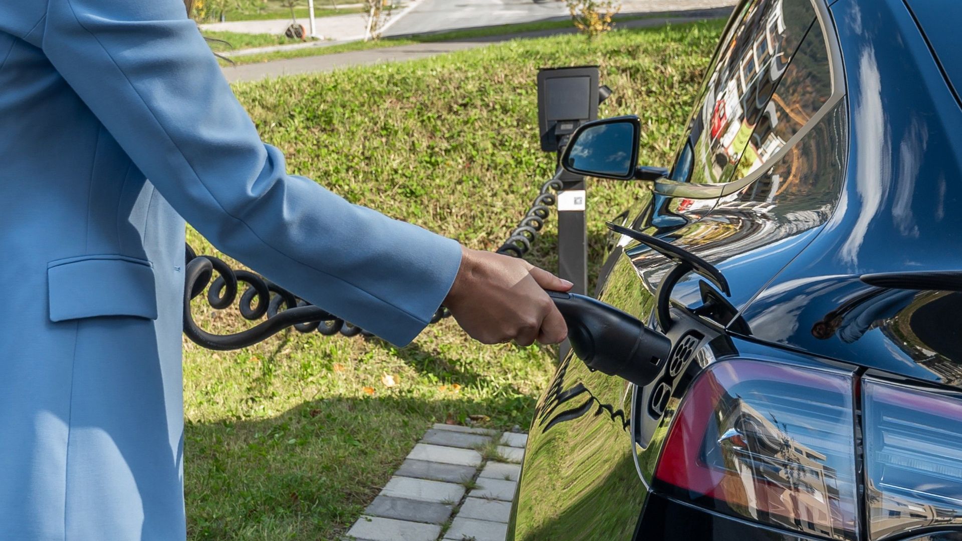 Person connecting an electric car to a charging station outdoors, showcasing green energy transition.