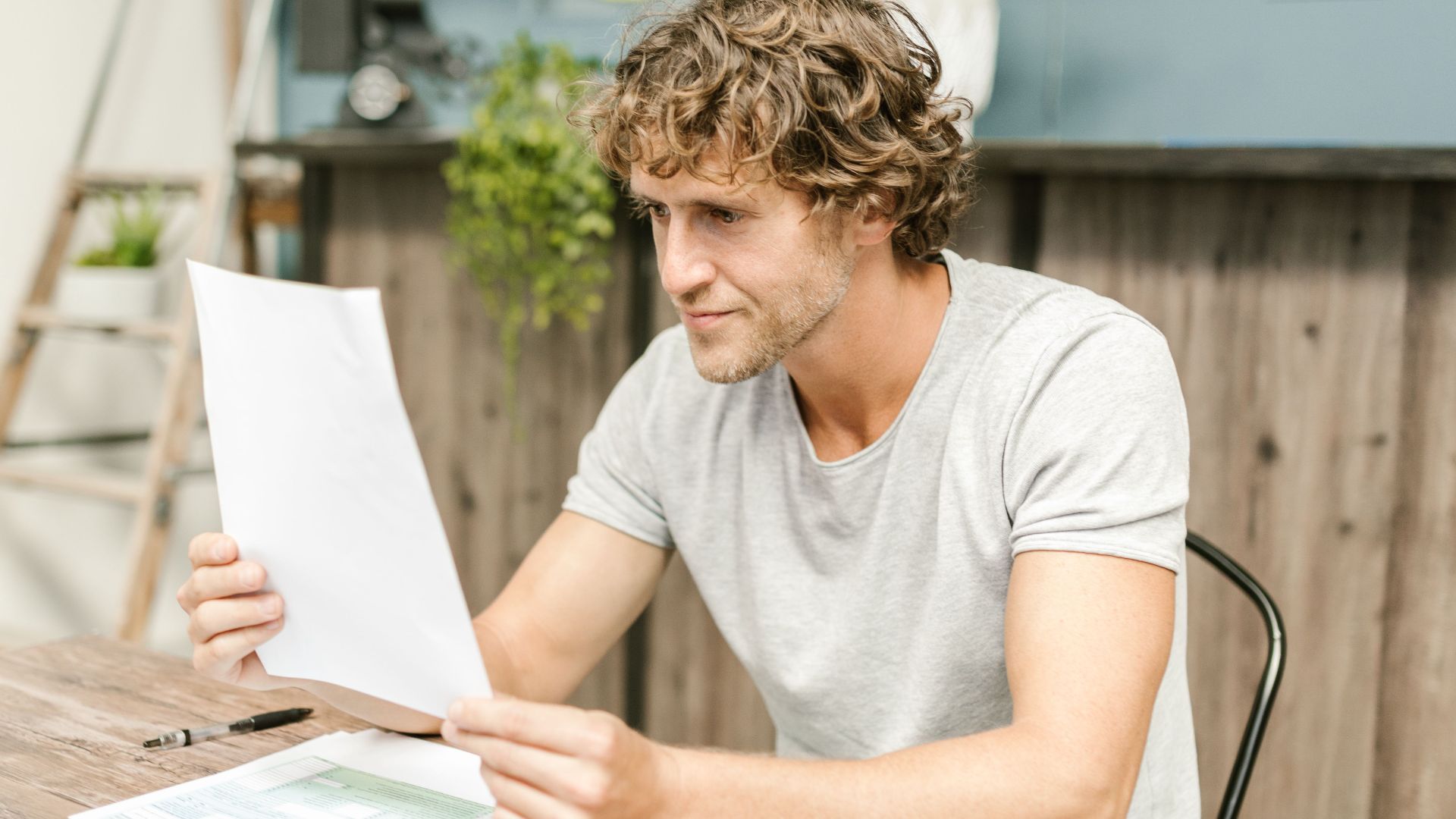 A man with curly hair evaluates documents at a desk, highlighting focused work in a professional setting.