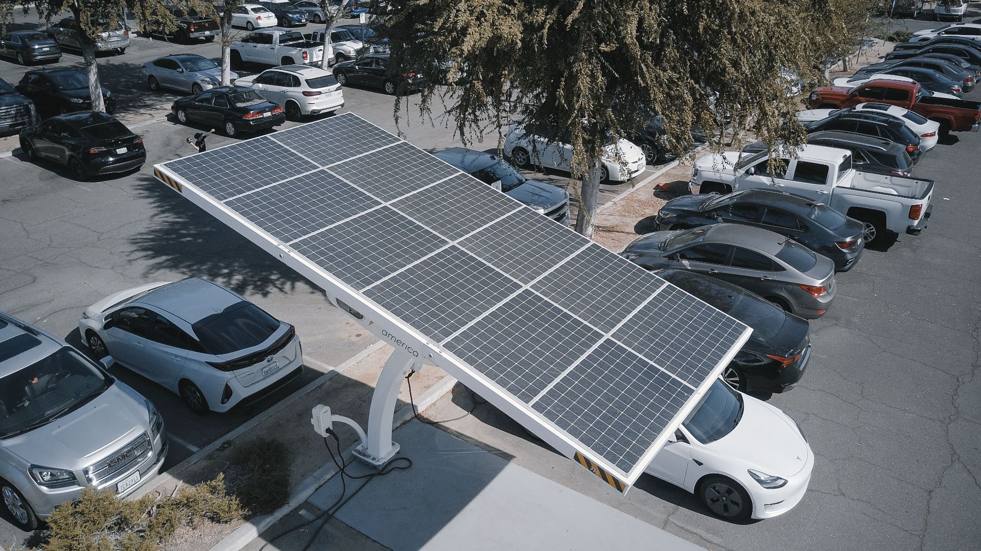 Electric cars charging at a solar-powered station in a parking lot.