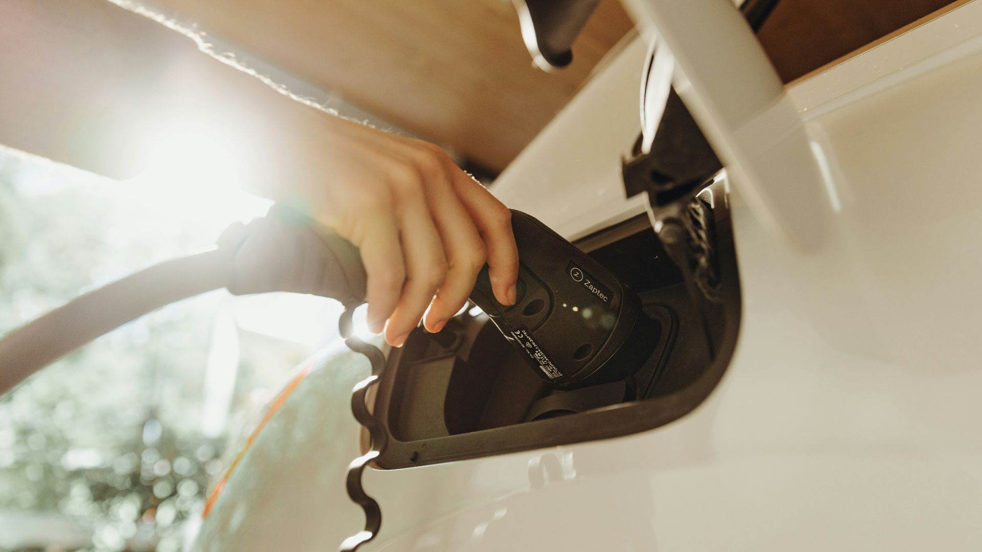A hand plugging a charging cable into a white electric vehicle