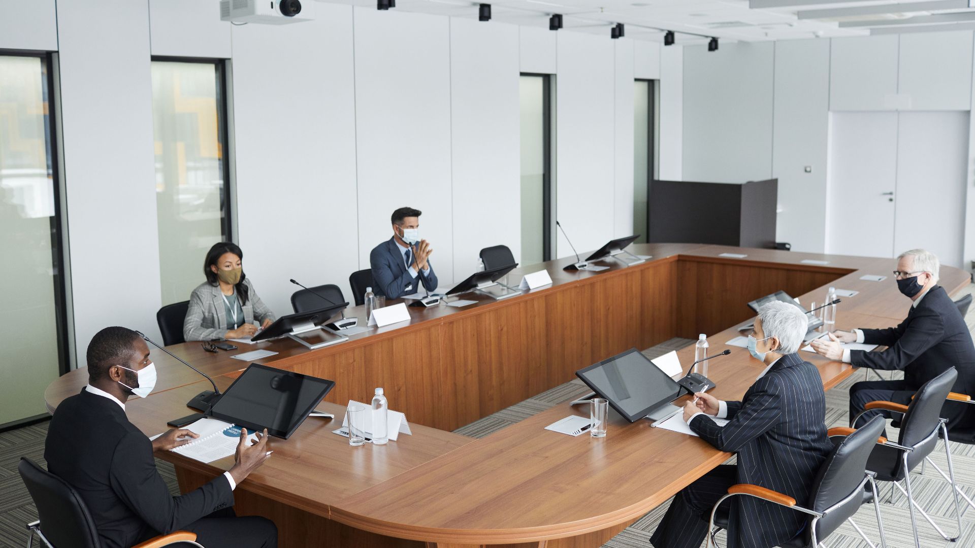 Business professionals wearing masks attending a conference meeting in a modern setting.