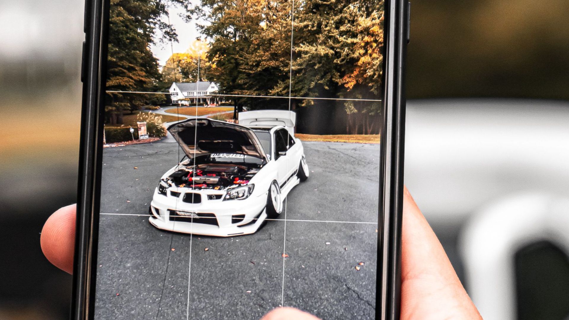 Person photographing a white car outdoors with a smartphone, showing technology and leisure.