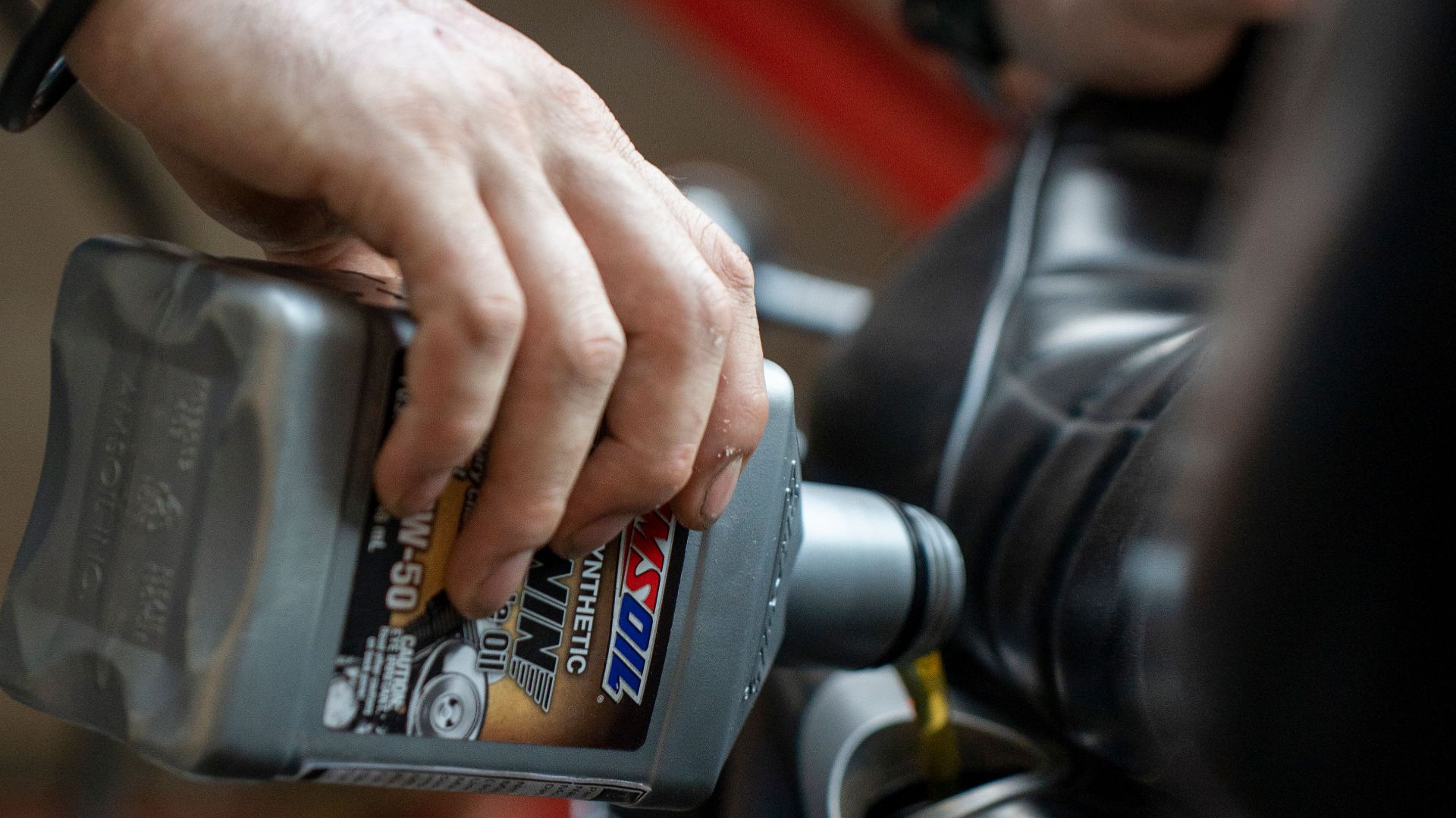 Close-up of a mechanic pouring engine oil into a motorcycle inside a garage.