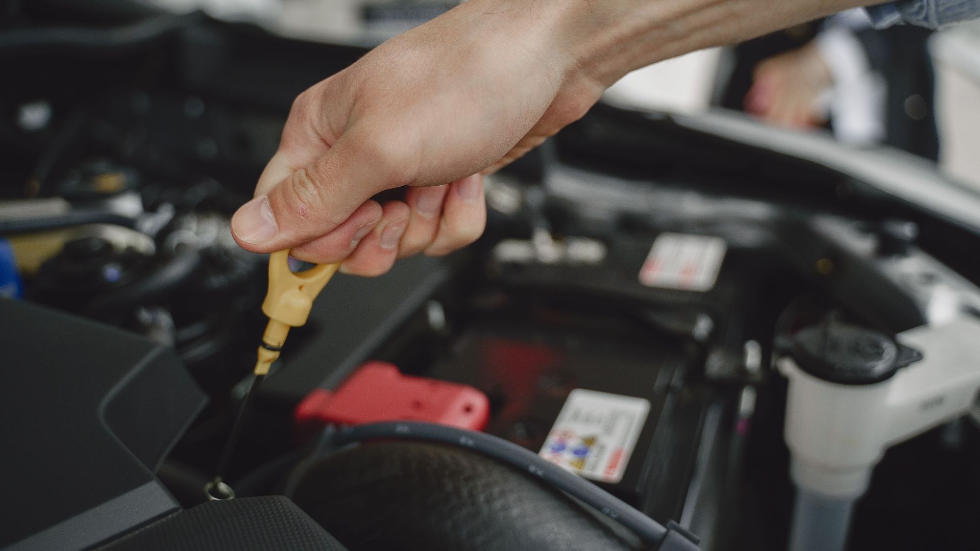Hand checking oil dipstick in a car engine bay for maintenance and diagnostics.