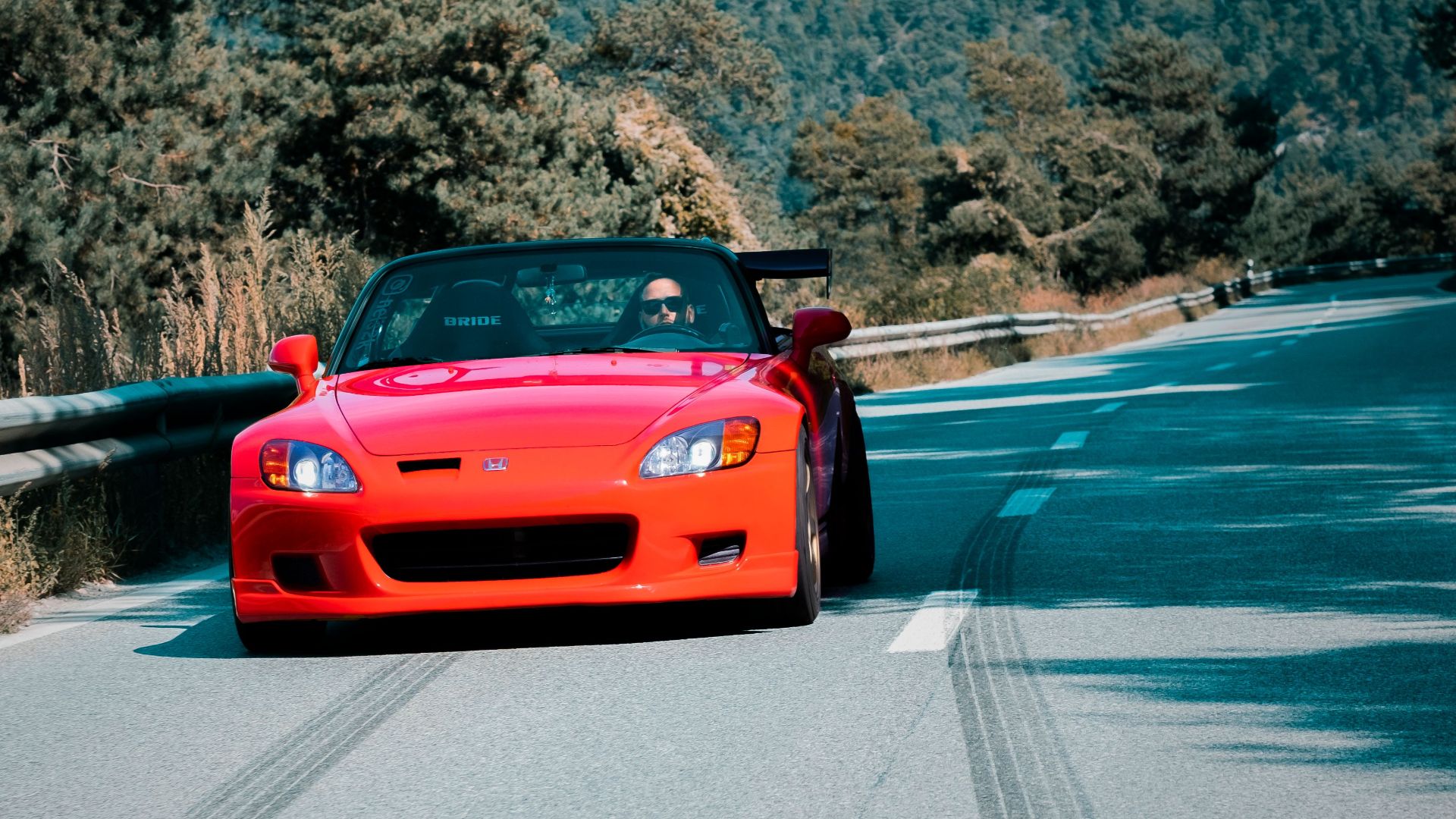 A vibrant red convertible speeds through a scenic mountain road in Sion, Switzerland, showcasing automotive elegance.