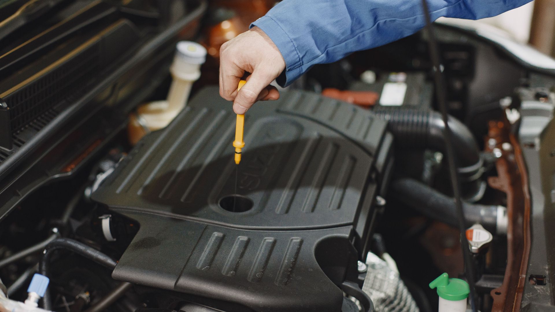 Close-up of a person checking engine oil using a dipstick in a car's engine bay.