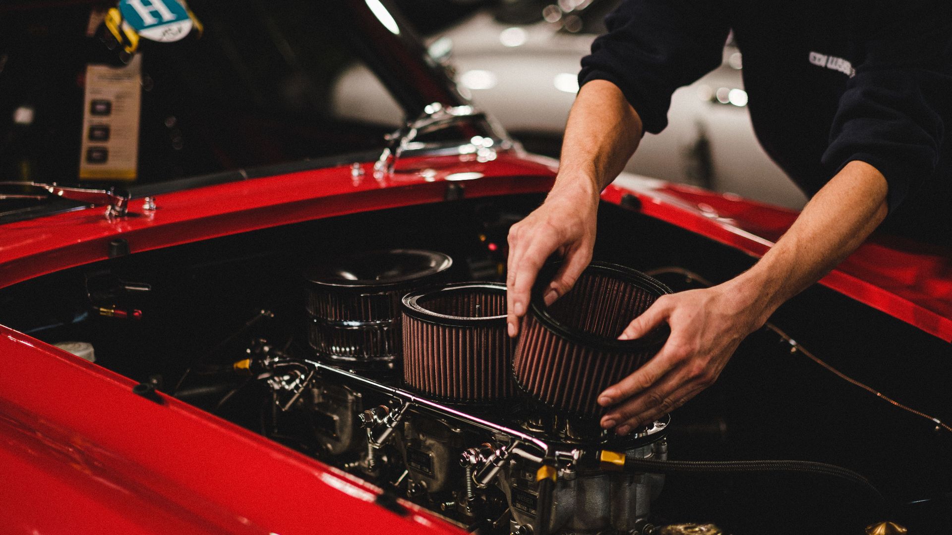 Close-up of a mechanic working on a car engine in a garage setting, focusing on air filter adjustment.