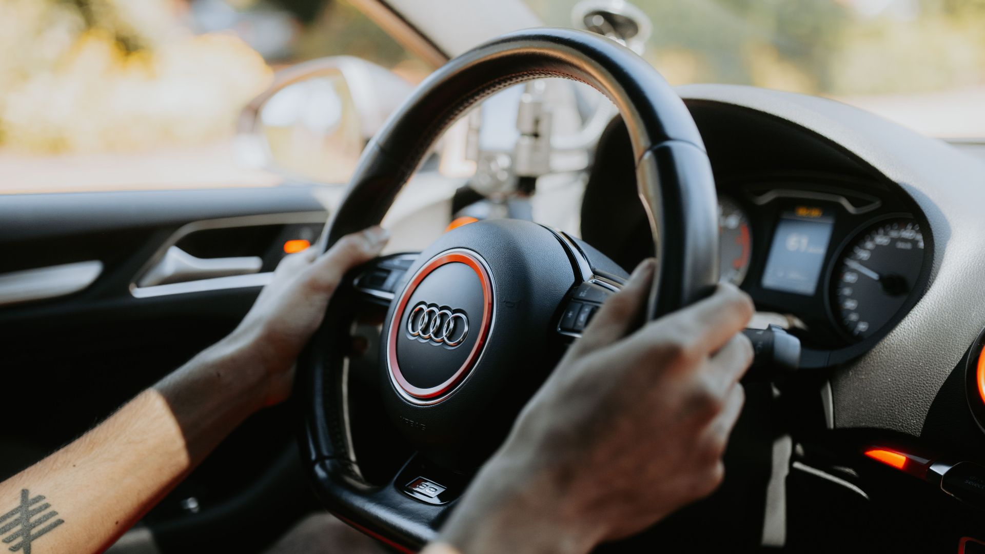 A close-up view of hands gripping a car steering wheel with dashboard visible.