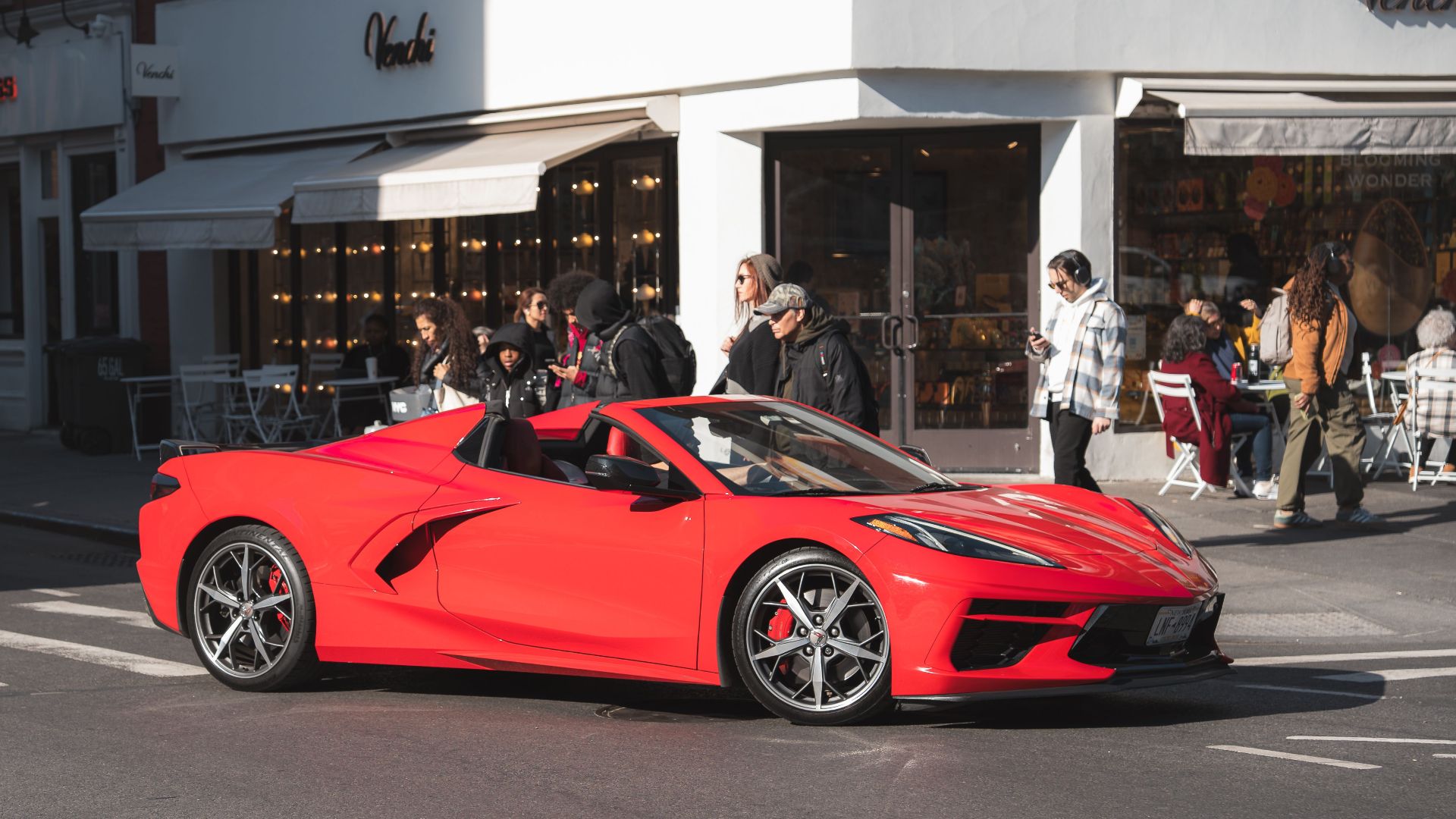 A sleek red convertible sports car parked on a bustling city street during the day.
