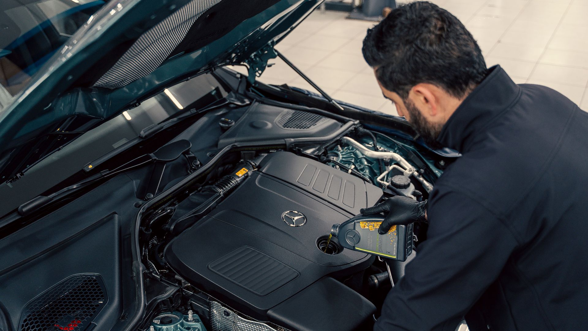 Mechanic inspecting and filling engine oil in a car at an indoor service center.